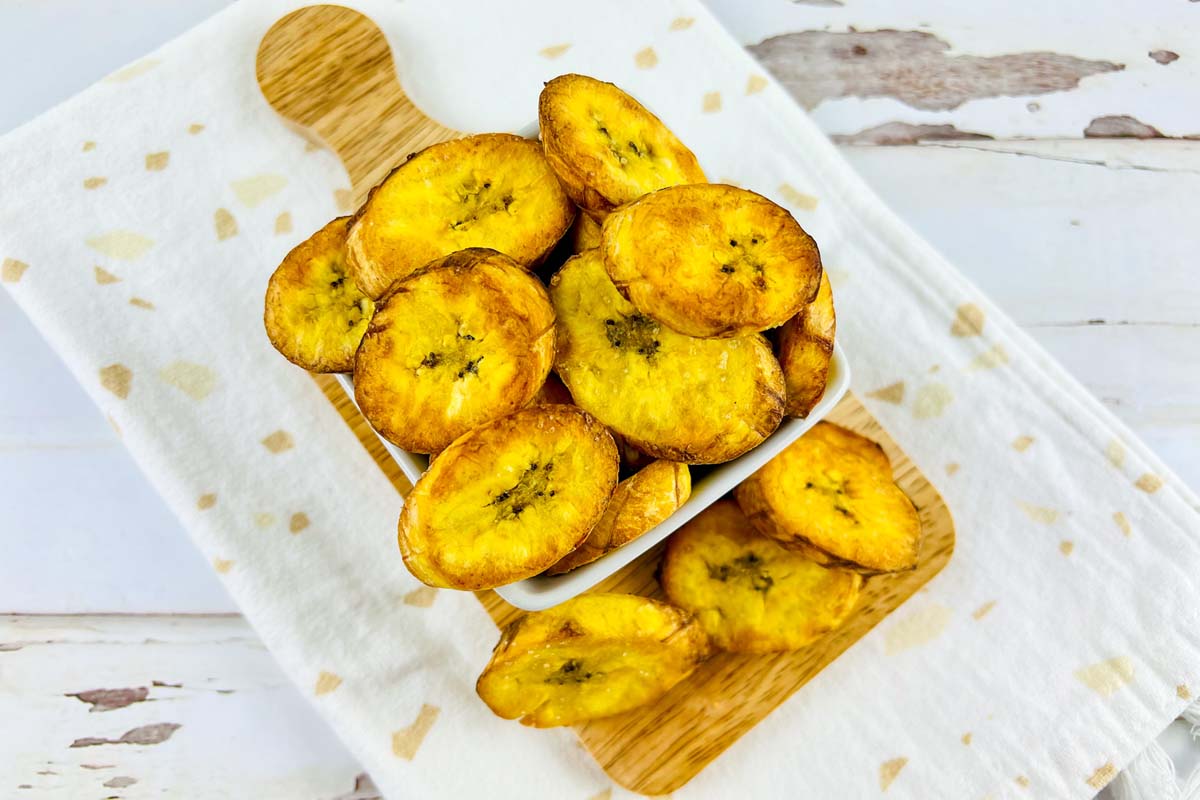 Plantains in a white bowl set on a wood board.