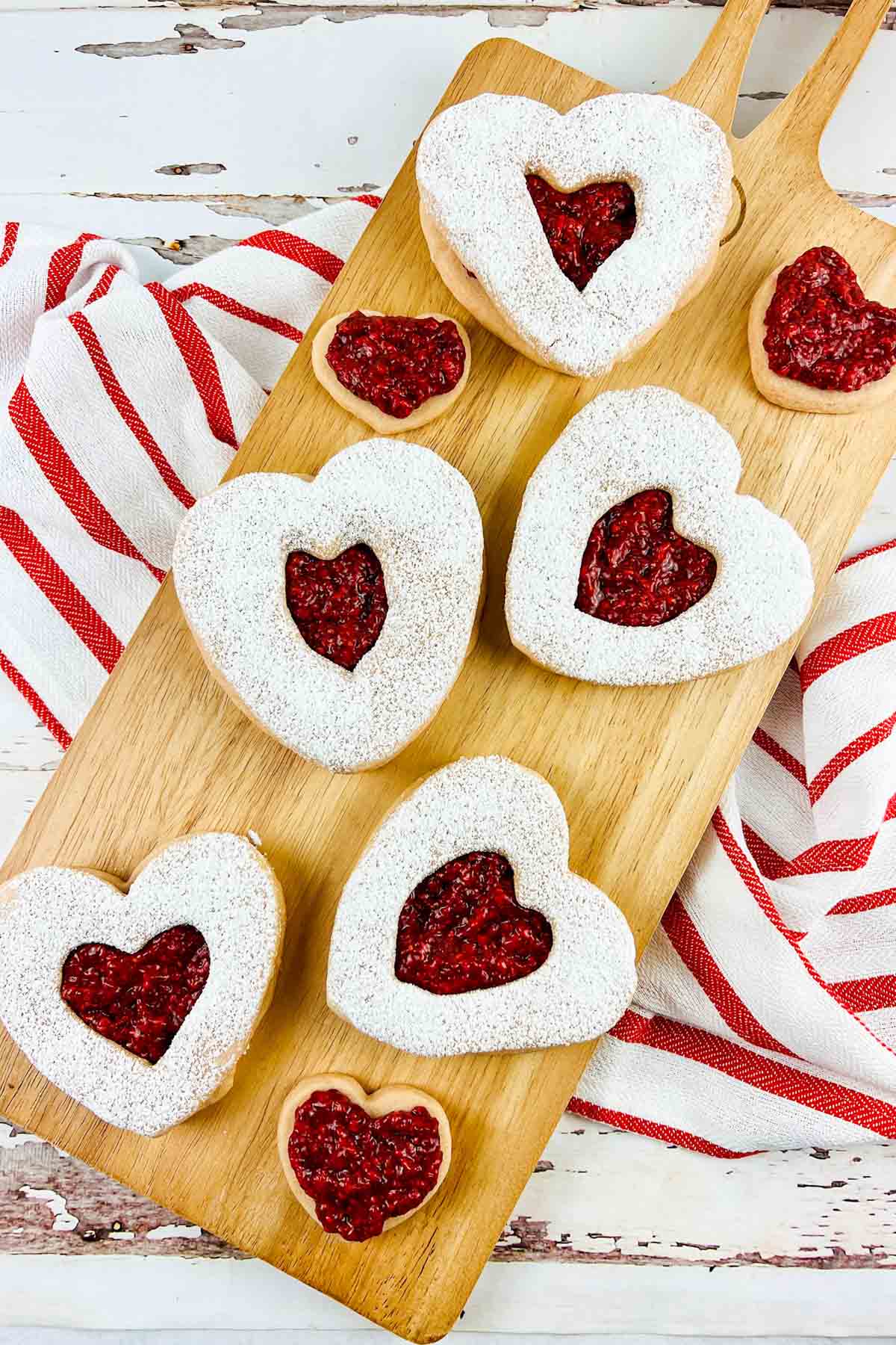 Heart shaped cookies on a board that is set on a kitchen towel.