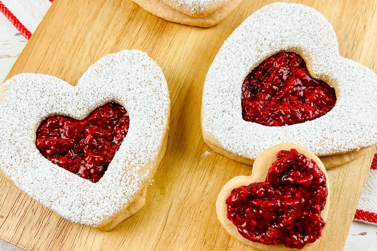 Two heart shaped cookies on a cutting board.