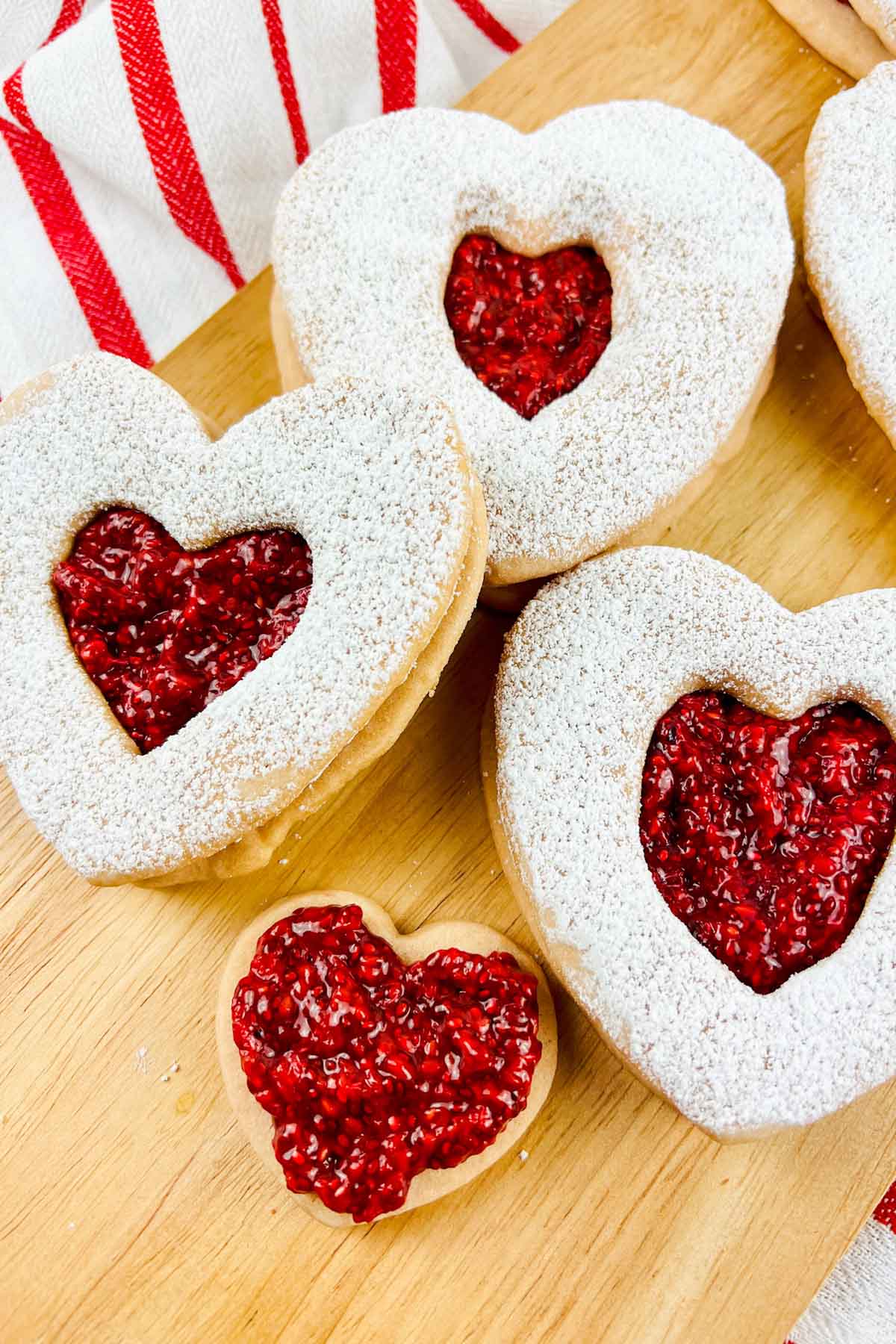 close up view of jam filled heart shaped cookies on a wood board.