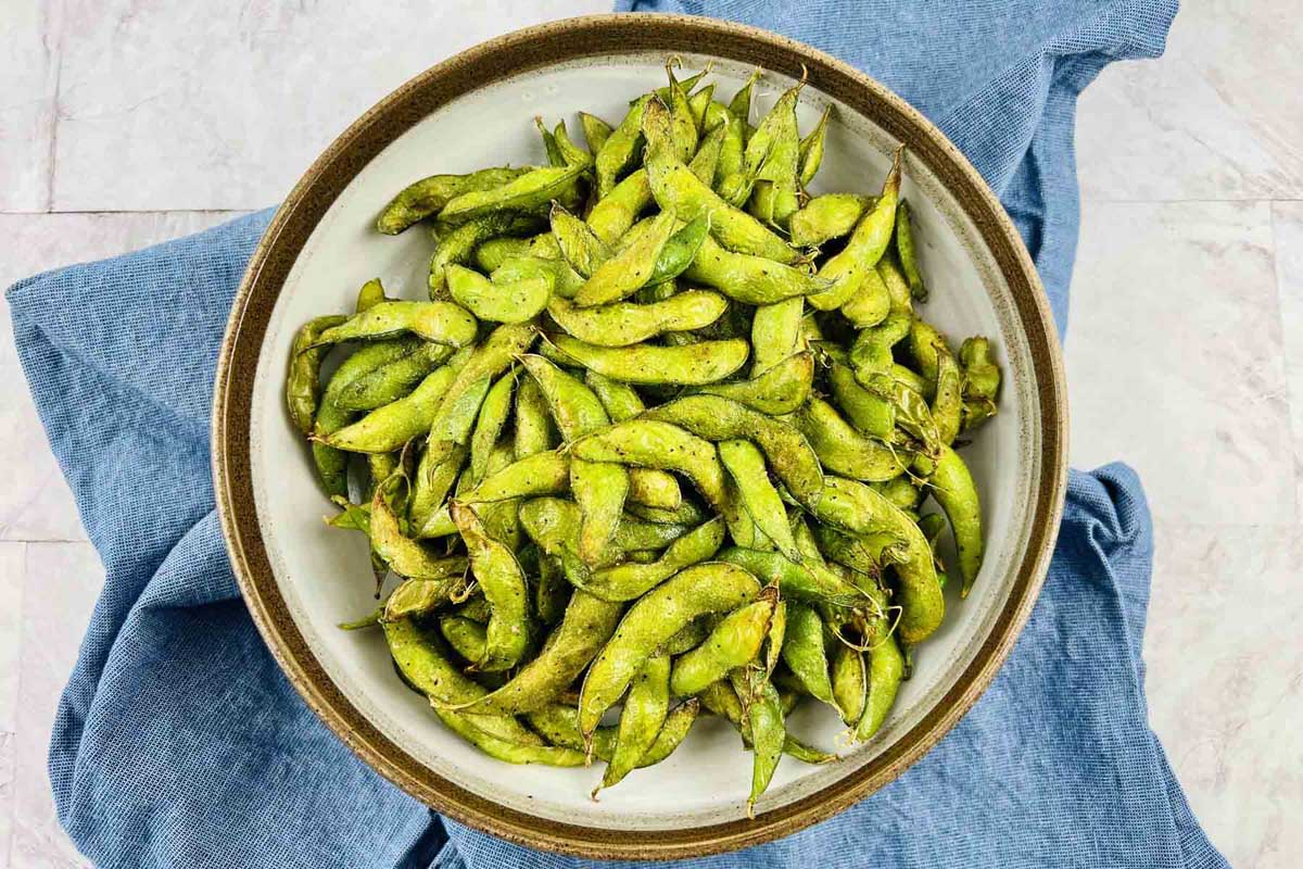 Cooked edamame in a bowl set on a blue kitchen towel.