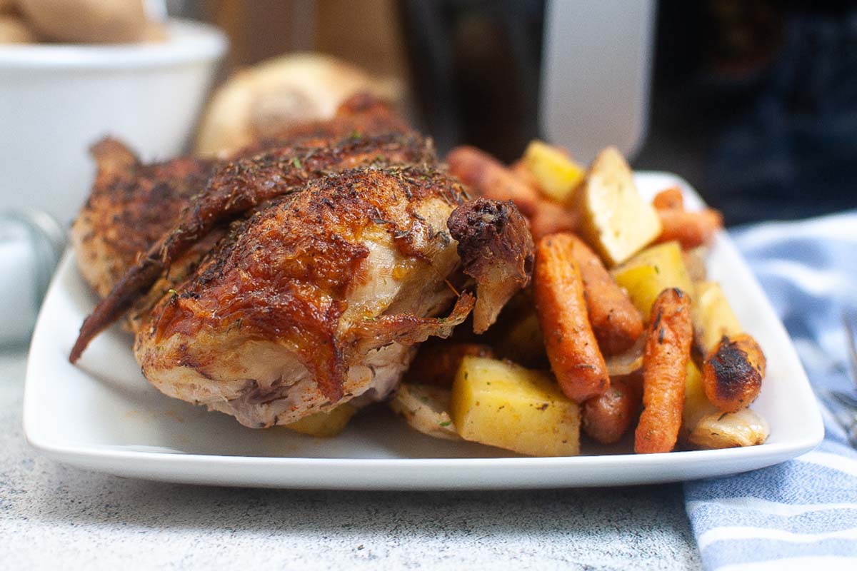 Roasted chicken on a white plate with vegetables.