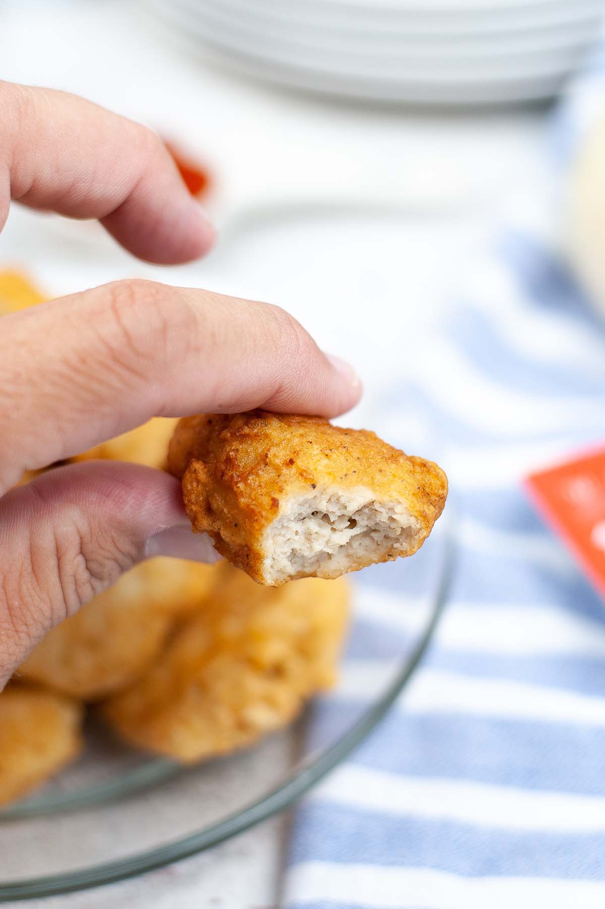 Hand holding a chicken nugget that has a bite taken out.