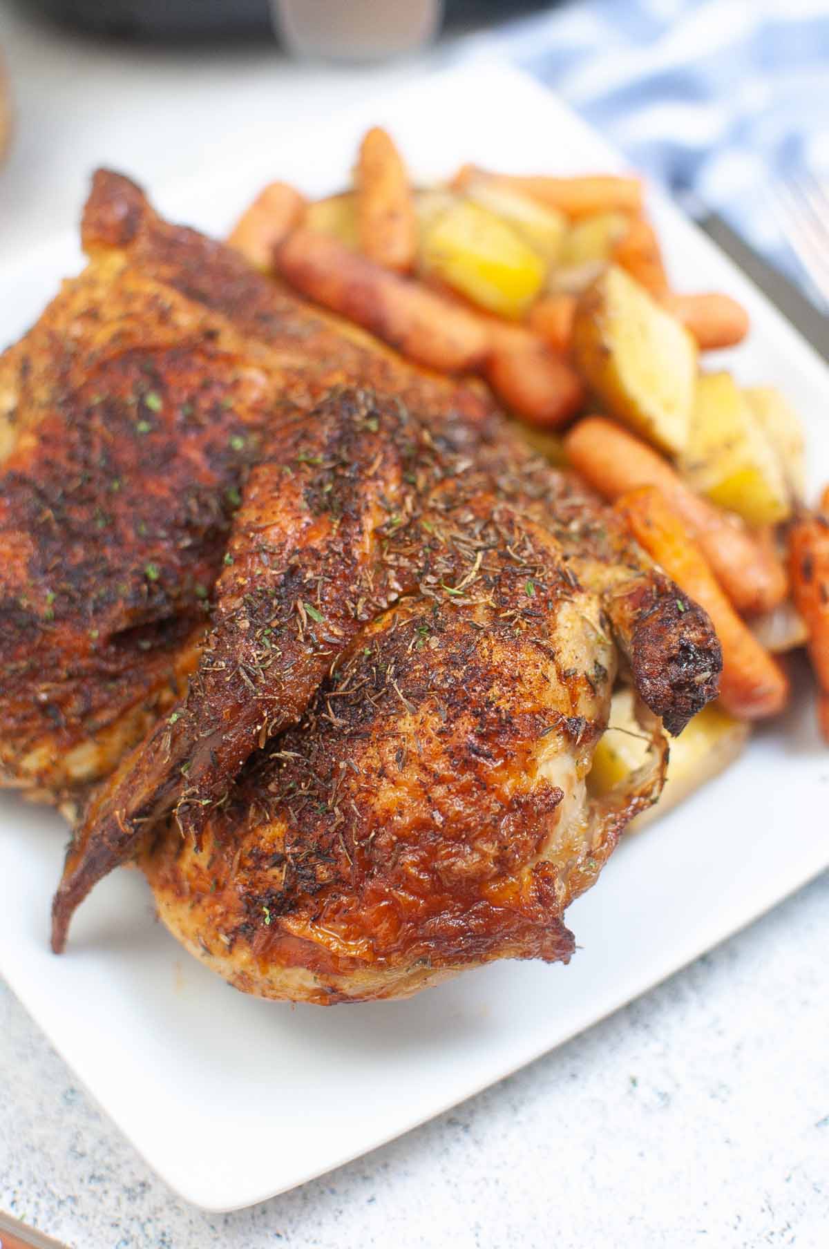 Cooked half chicken on a plate with carrots and potatoes.