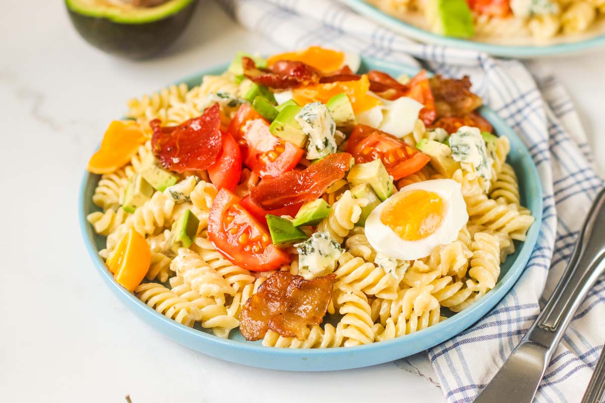 Pasta salad topped with bacon, eggs, tomatoes and cheese.