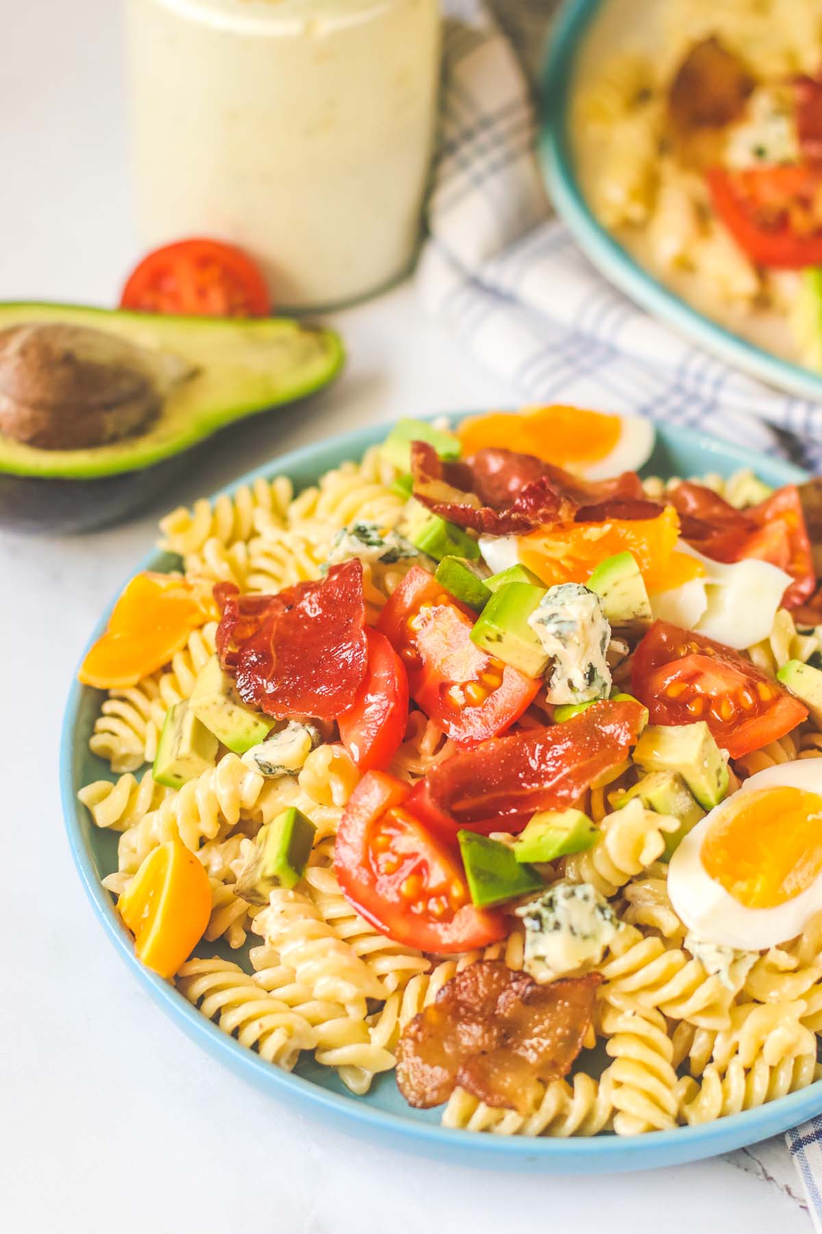 Pasta salad on a blue plate next to an avocado cut in half.