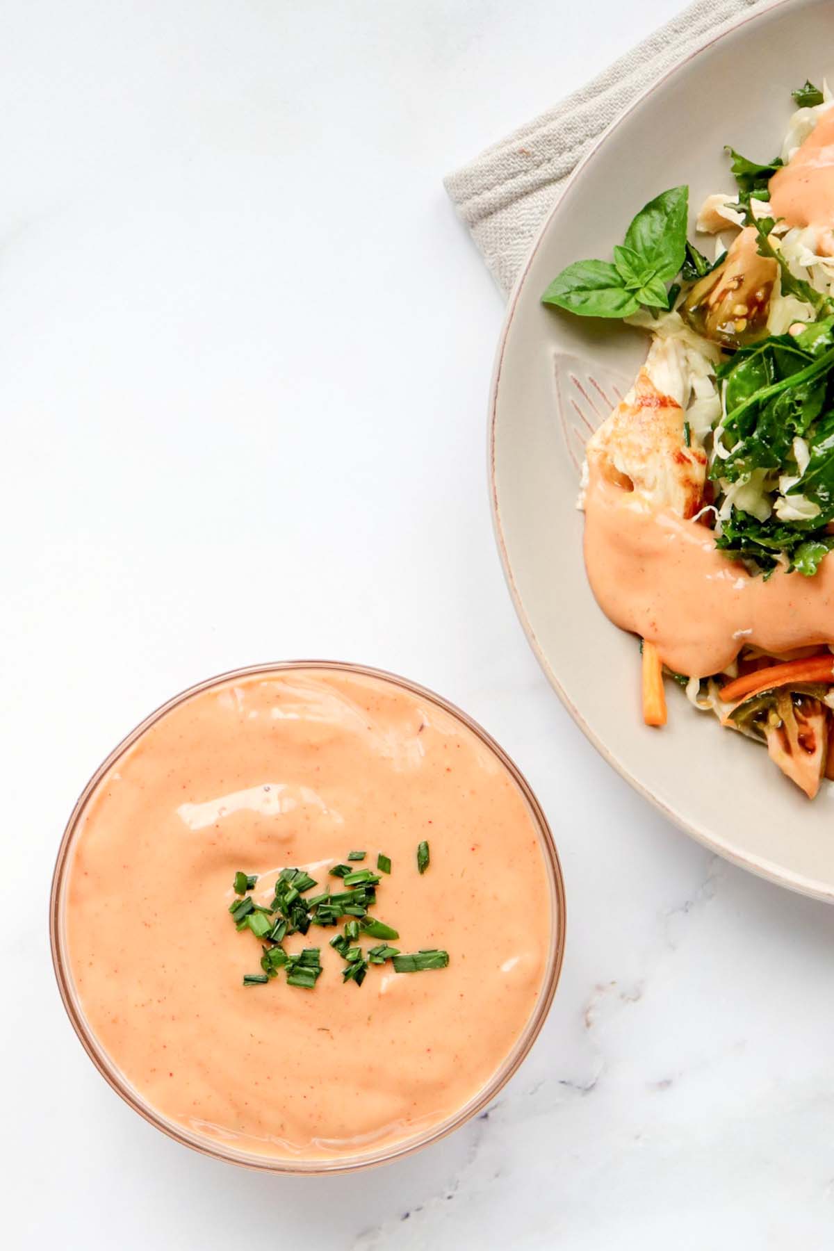 Dressing in a bowl next to a plate of salad.