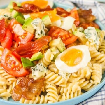 Pasta salad topped with bacon, eggs, tomatoes and cheese.