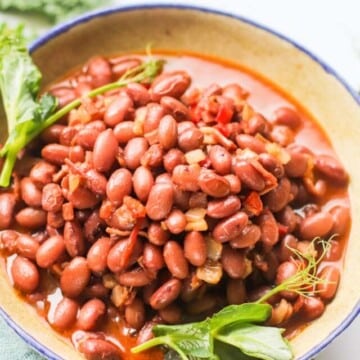 Beans in a bowl topped with green leaves.