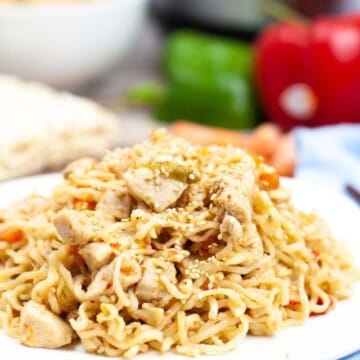 Ramen noodles topped with chicken on a white plate.
