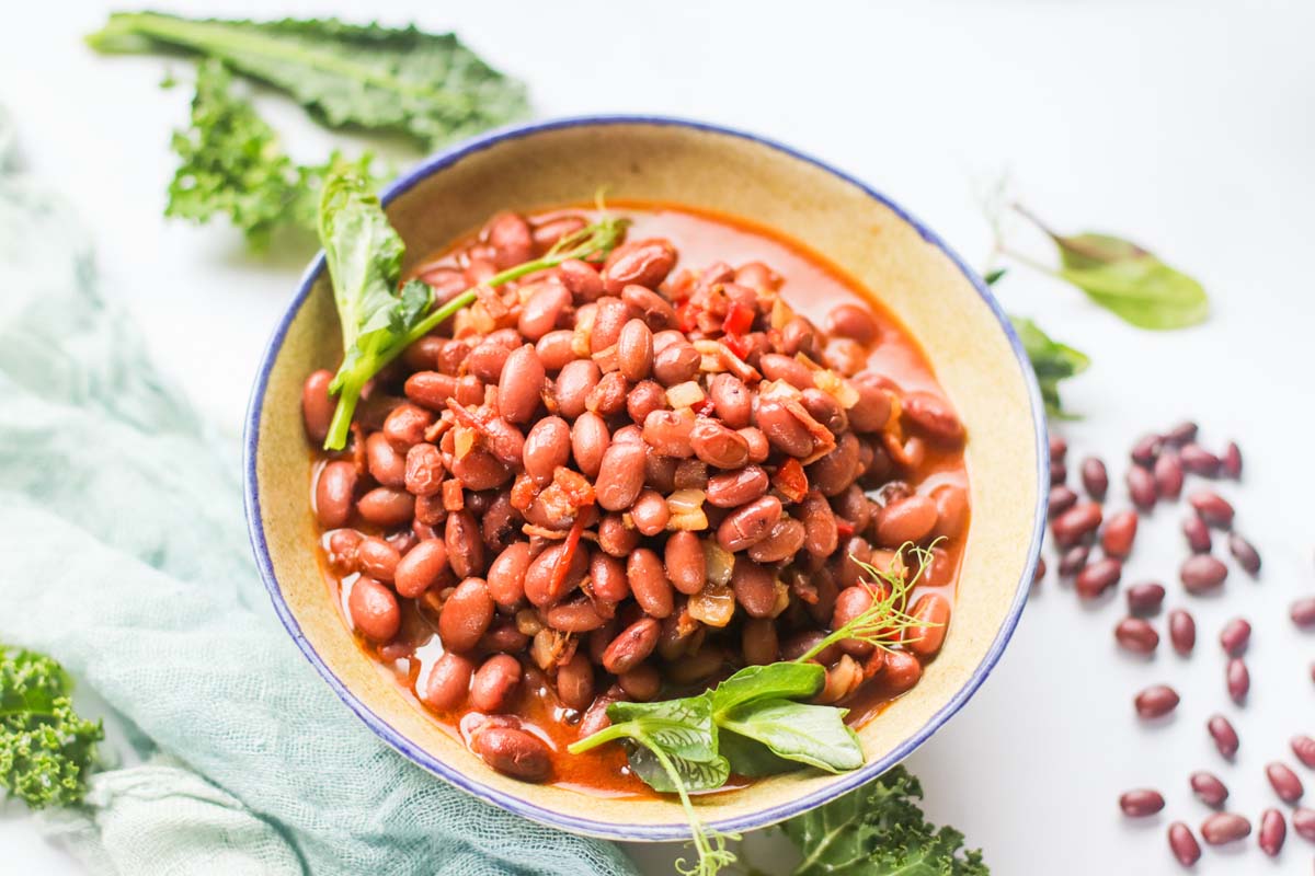 Beans in a bowl topped with green leaves.