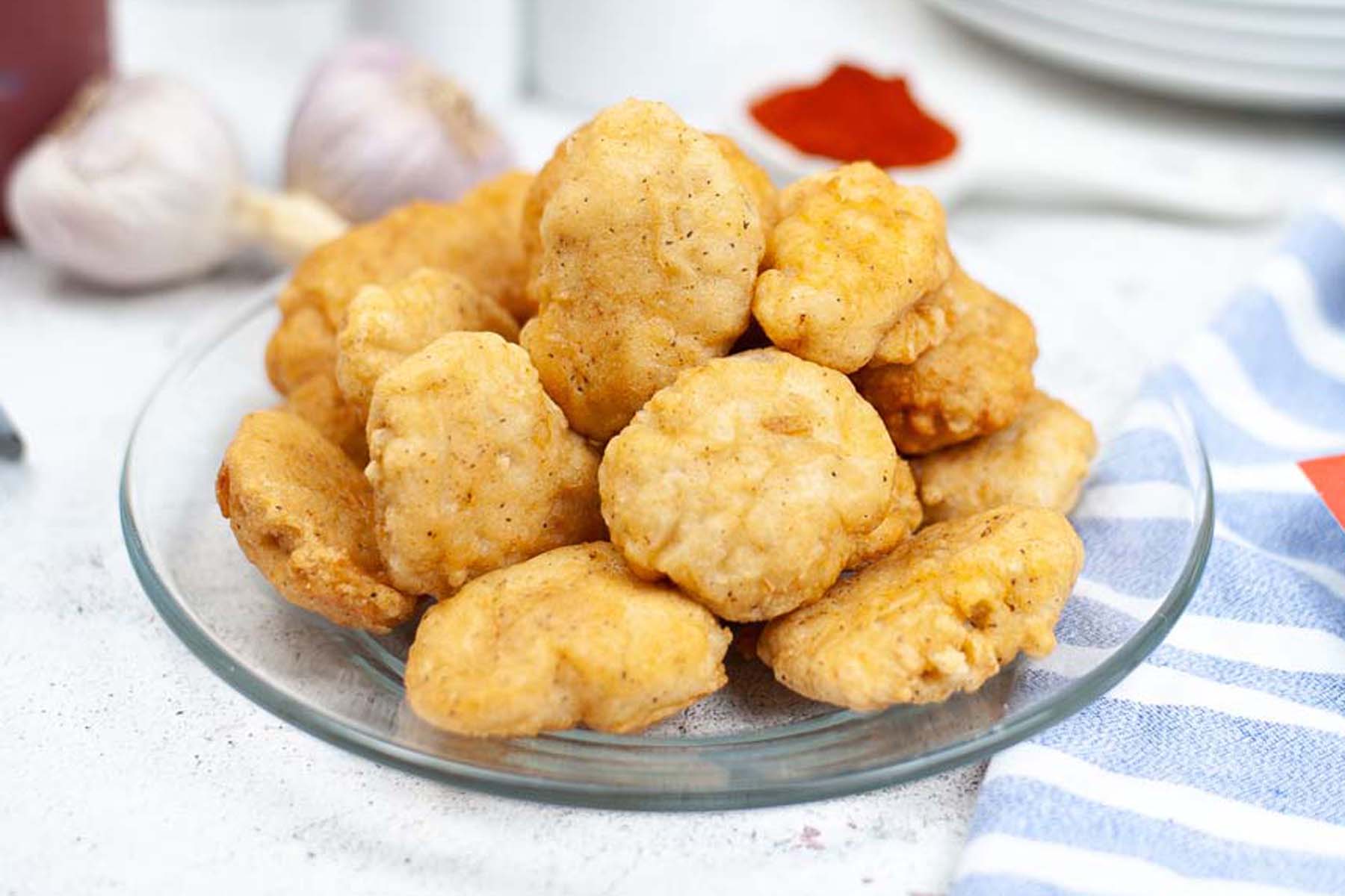 Chicken nuggets piled on a clear plate.