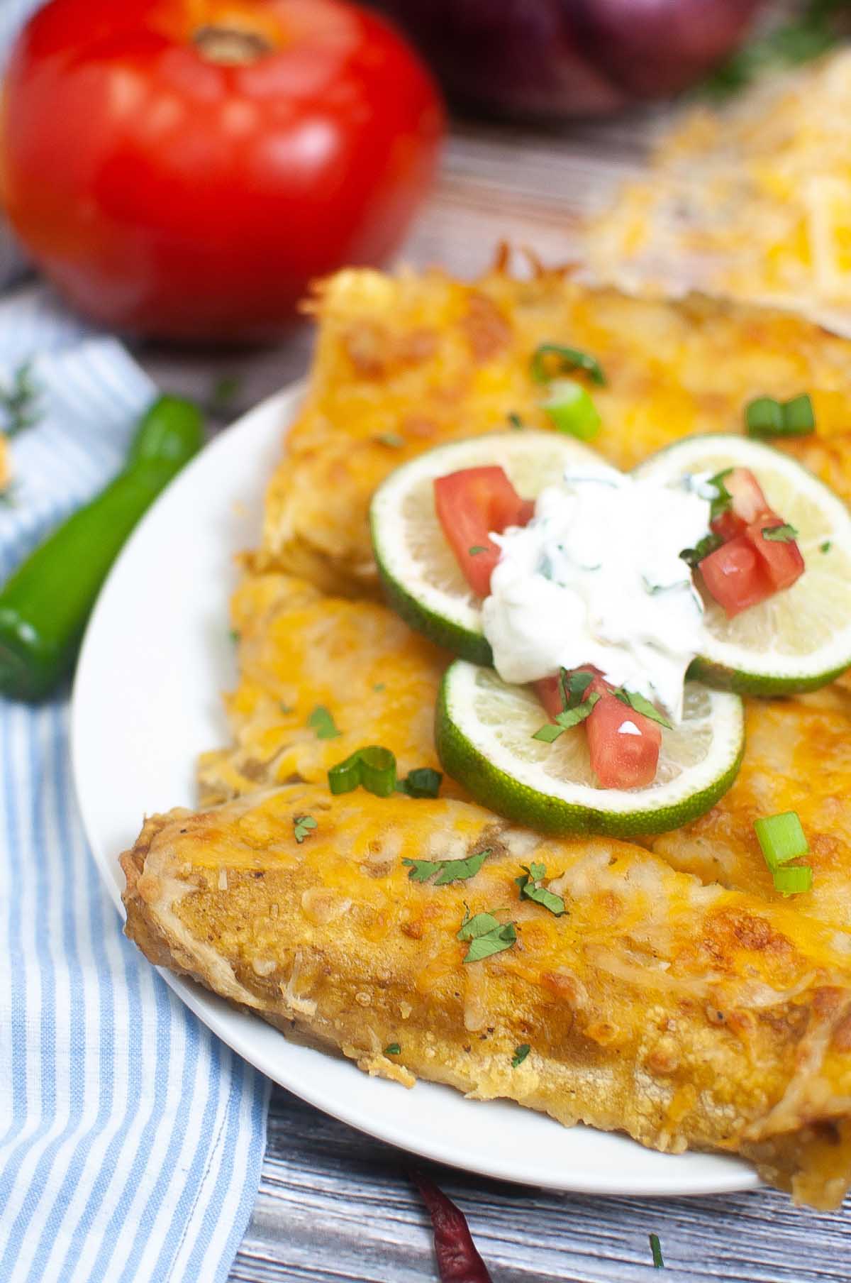Enchiladas on a plate topped with lime slices and sour cream.