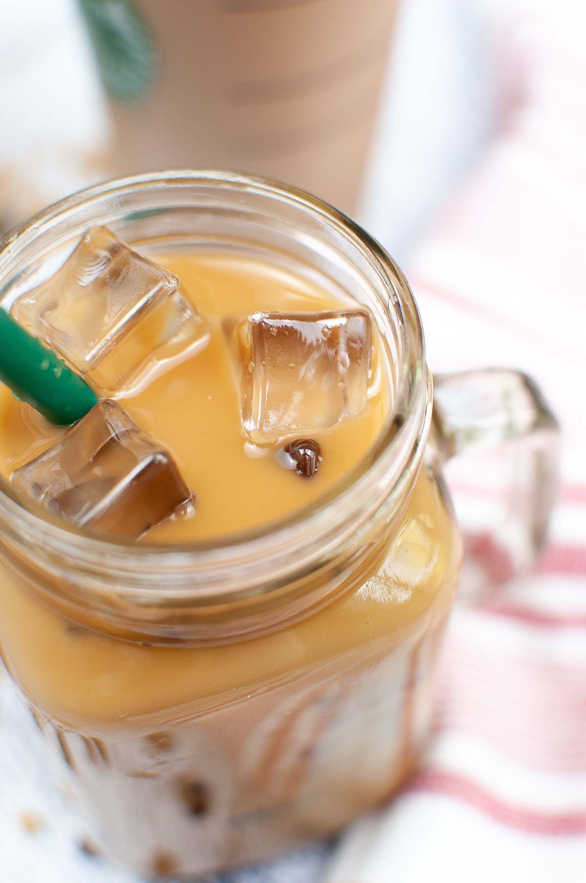 Coffee in a mason jar with ice cubes and a green straw.