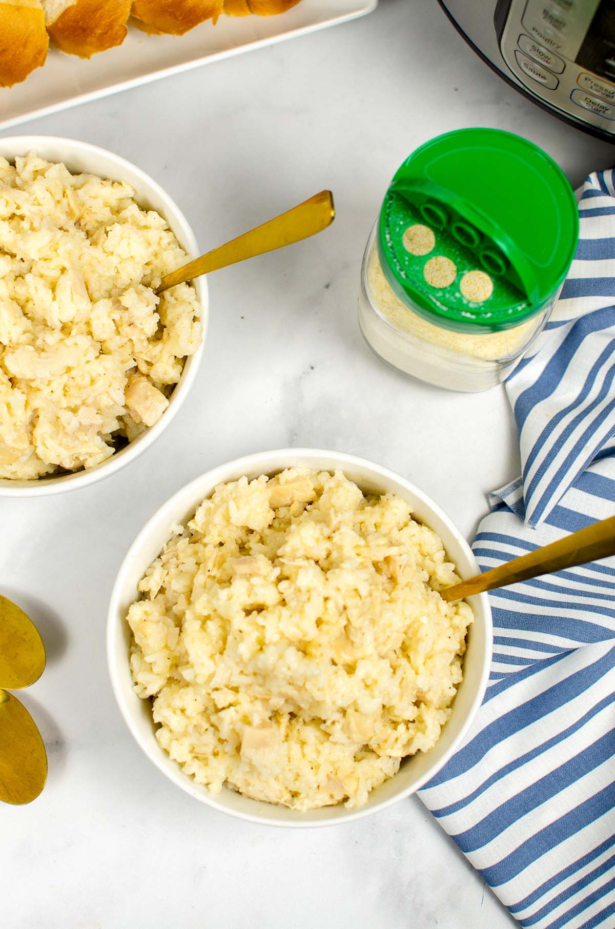 Two bowls of chicken and rice next to a jar of parmesan cheese.