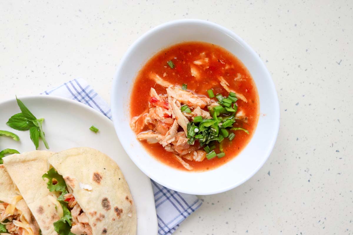 Shredded chicken in a bowl topped with sliced chives.