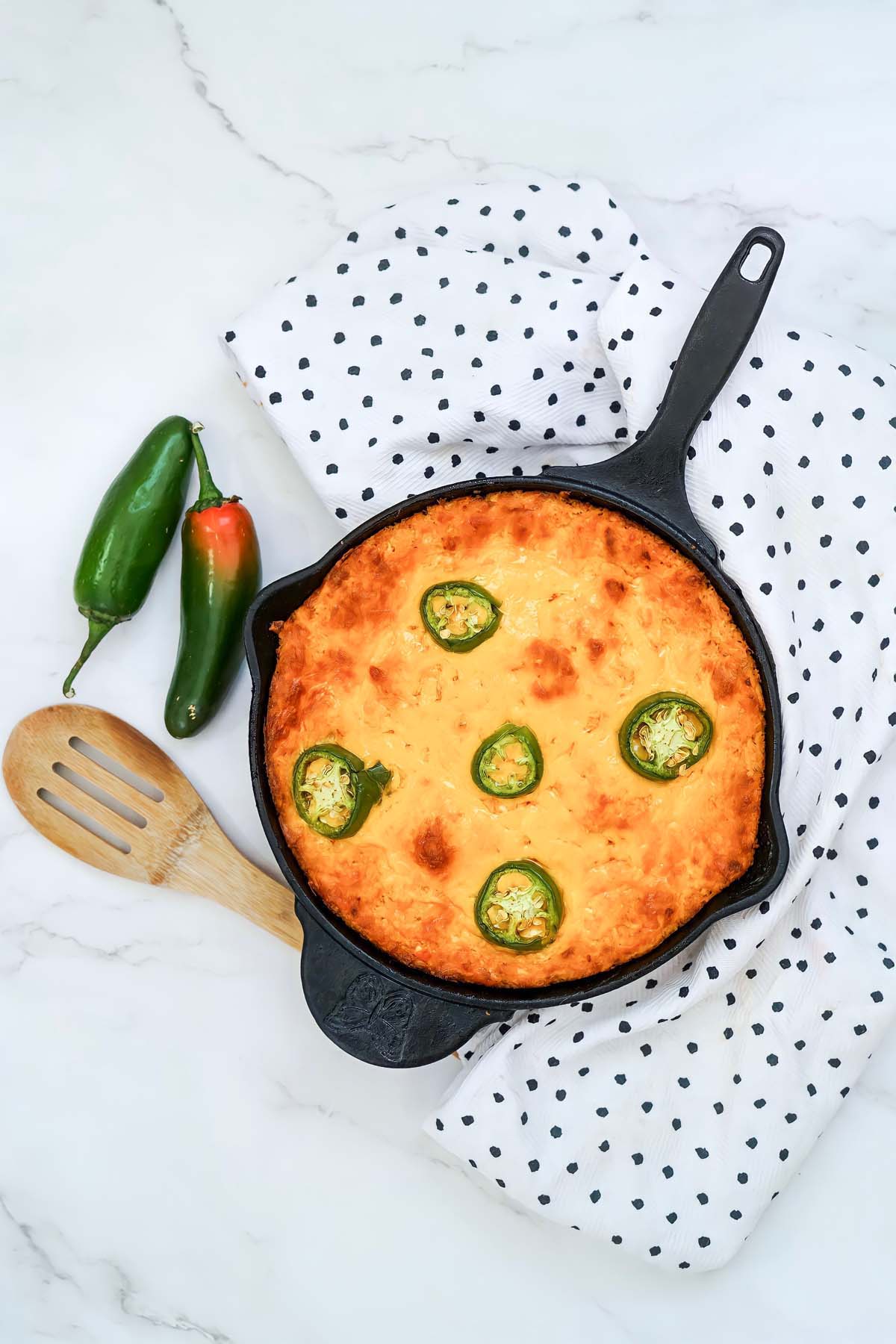 Cheese dip in a cast iron skillet next to a wooden spoon and two jalapeños.
