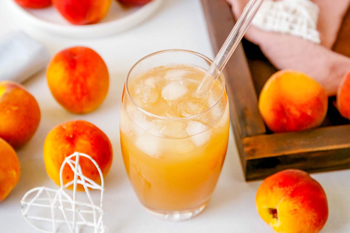 Peach tea in a glass with ice and a straw.