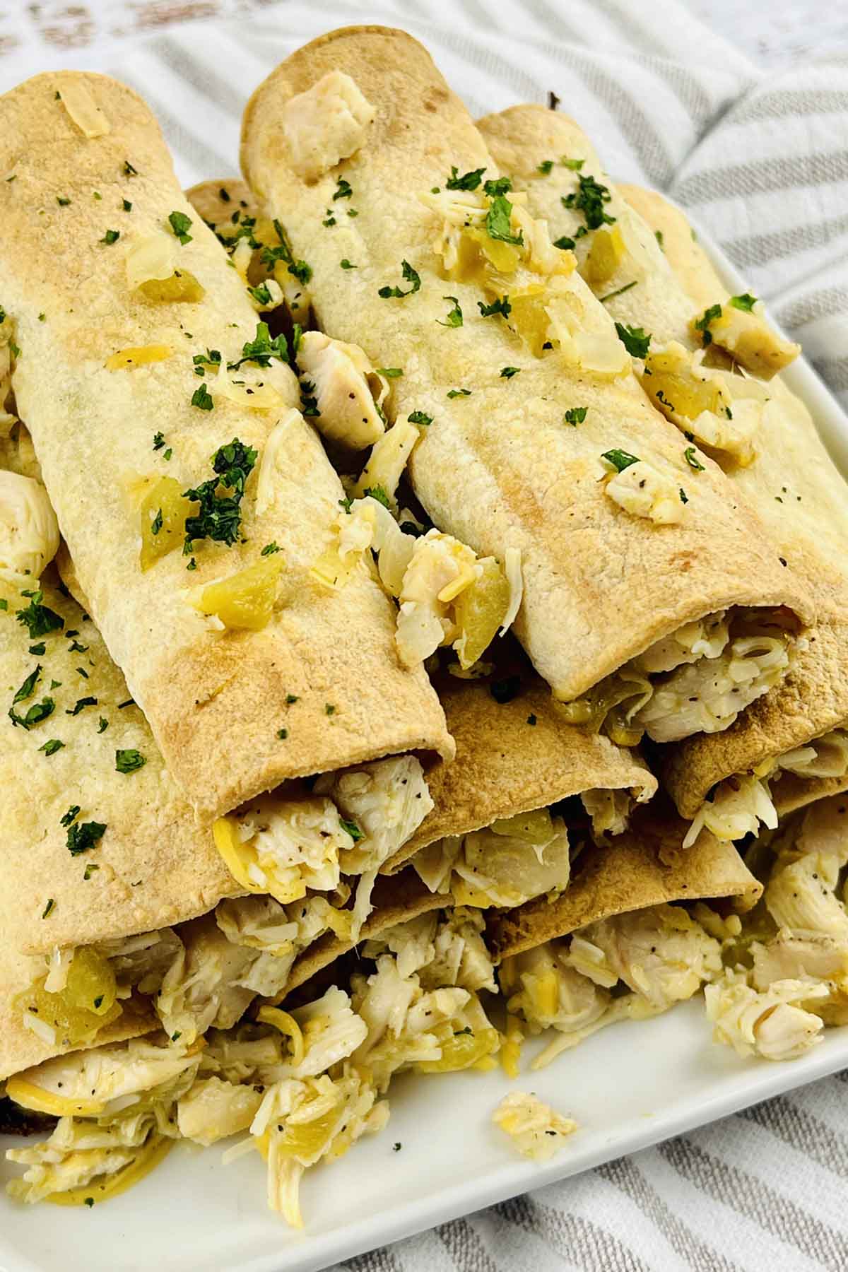 Taquitos stacked on a plate and sprinkled with chopped parsley.