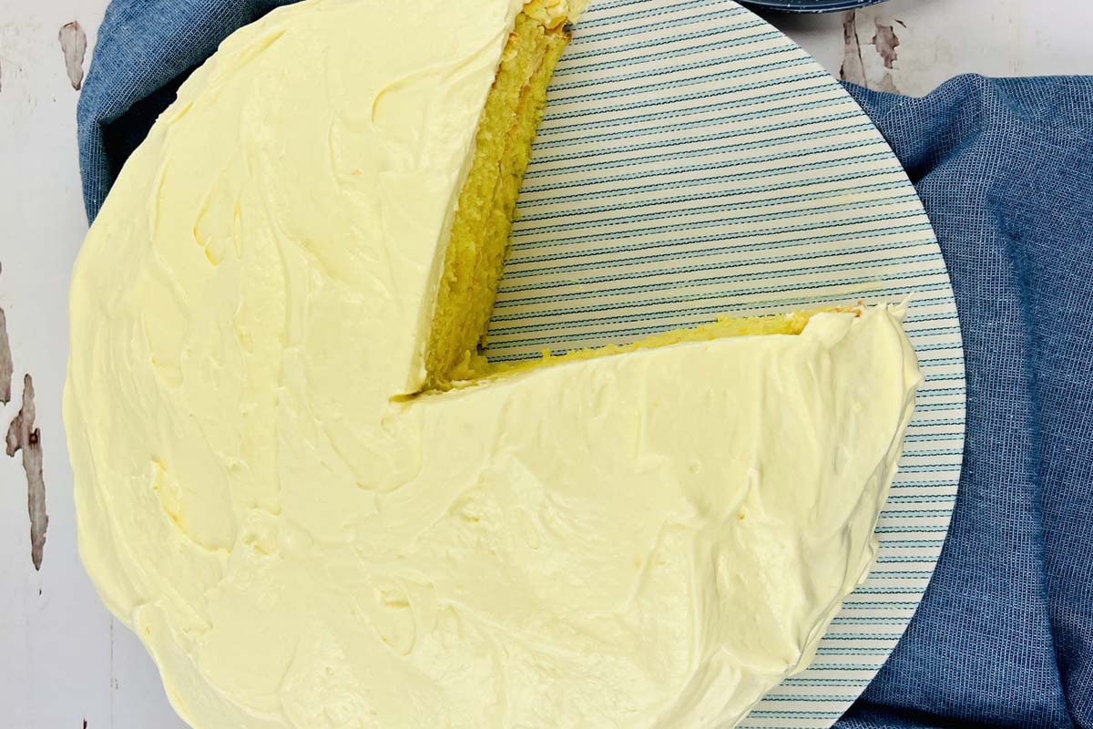 A frosted lemon cake with a slice taken out.