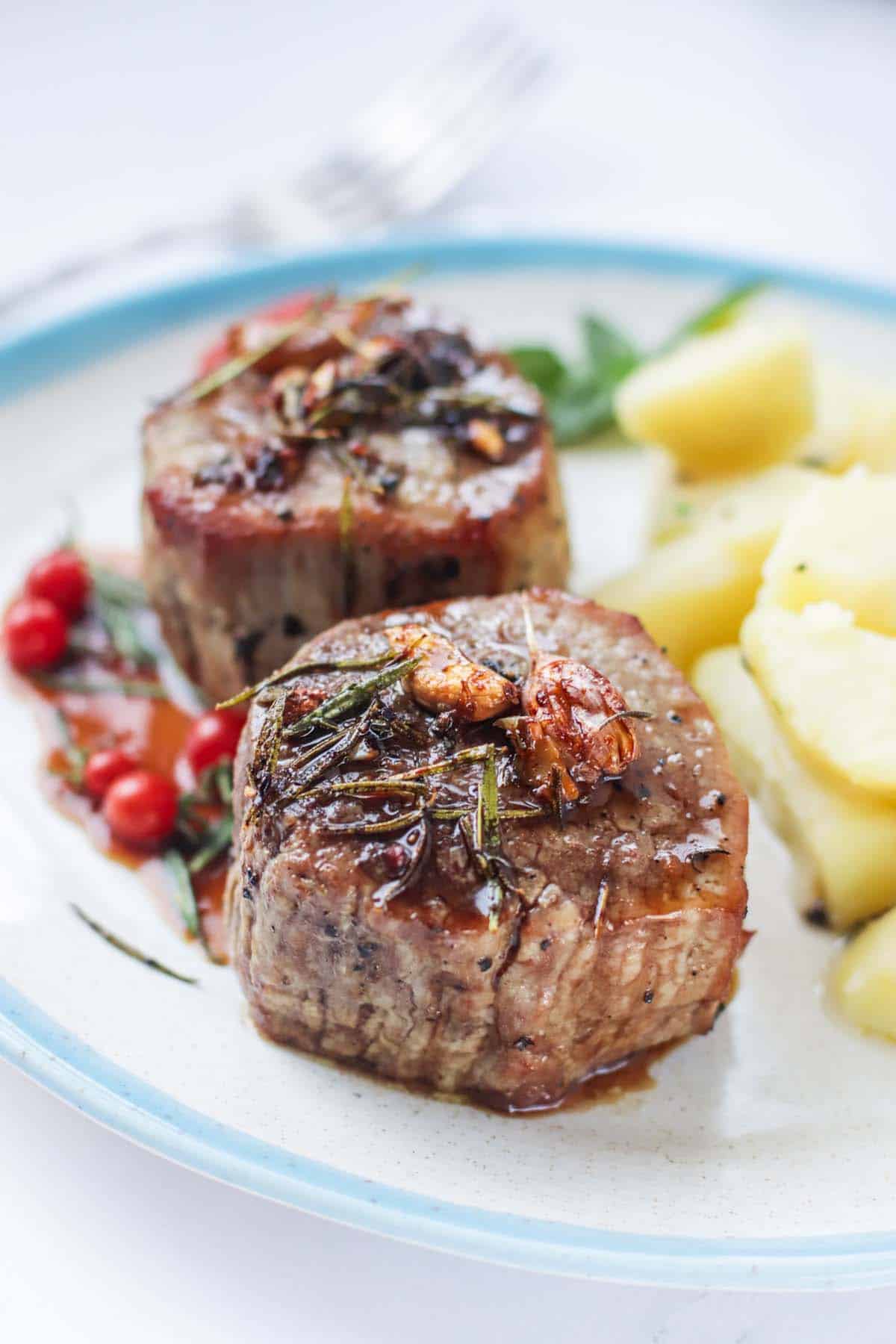Filet mignon on a plate topped with garlic and rosemary.