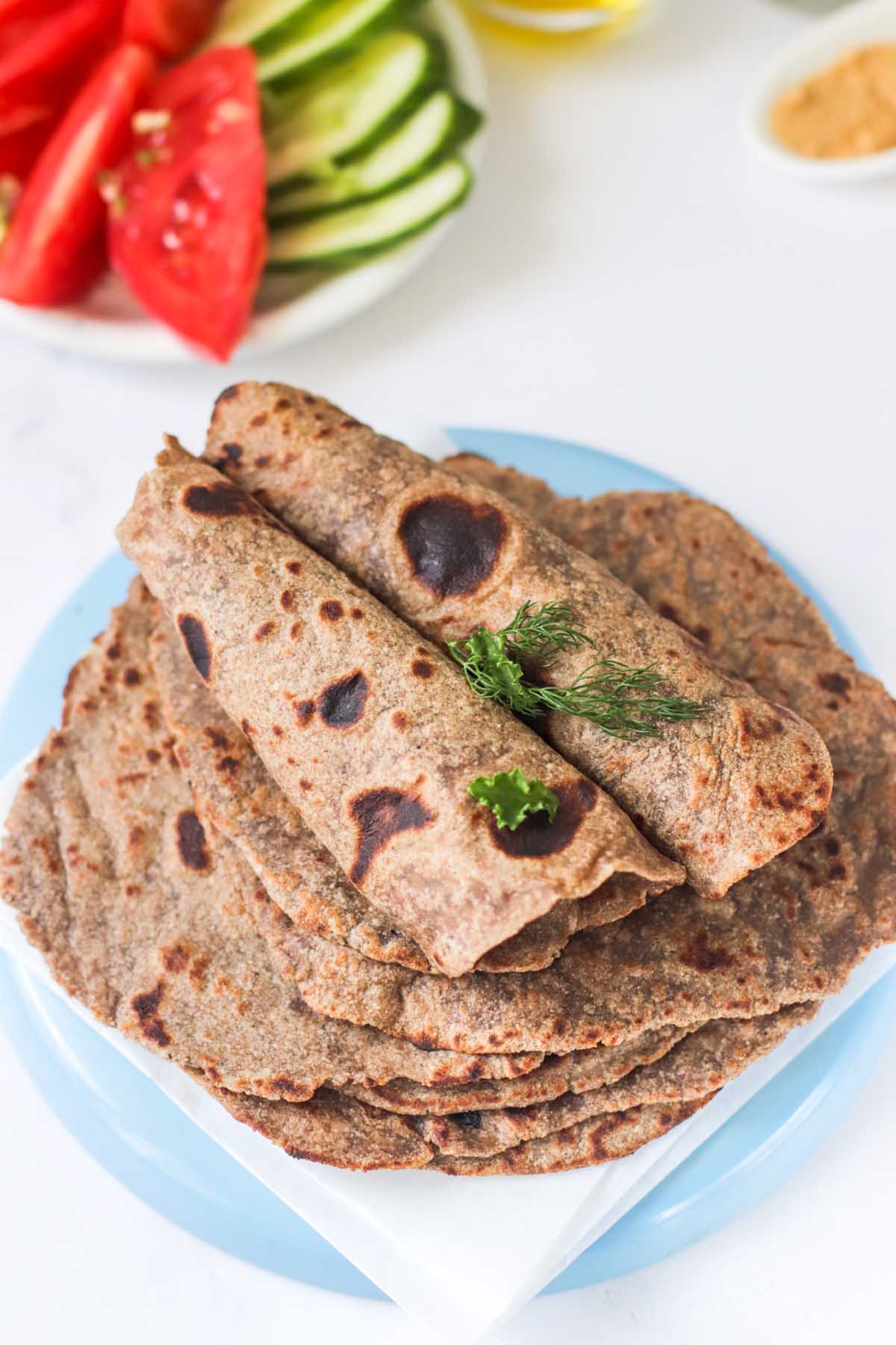 Stack of tortillas on a plate with two tortillas rolled on top.