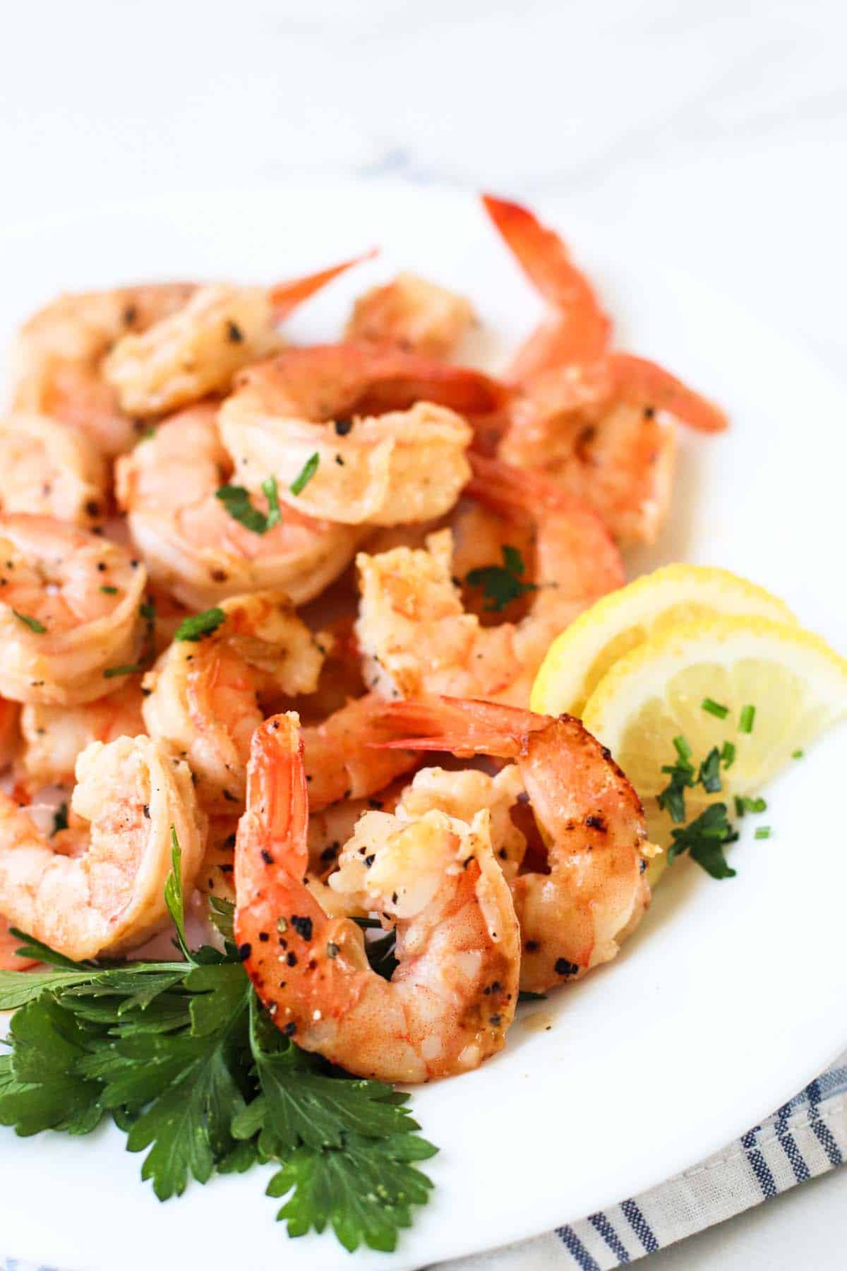 Cooked shrimp on a plate with lemon wedges.