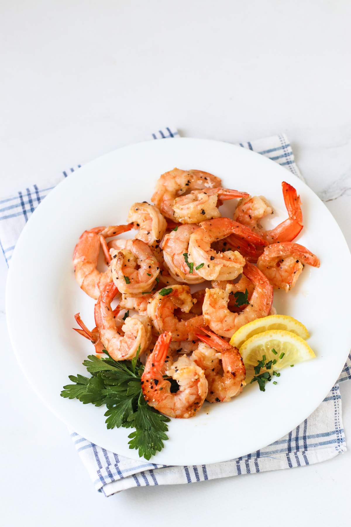 Cooked shrimp on a white plate garnished with parsley and lemon wedges.