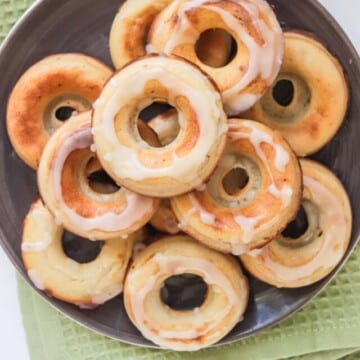 Donuts stacked on a black plate and set on a green kitchen towel.