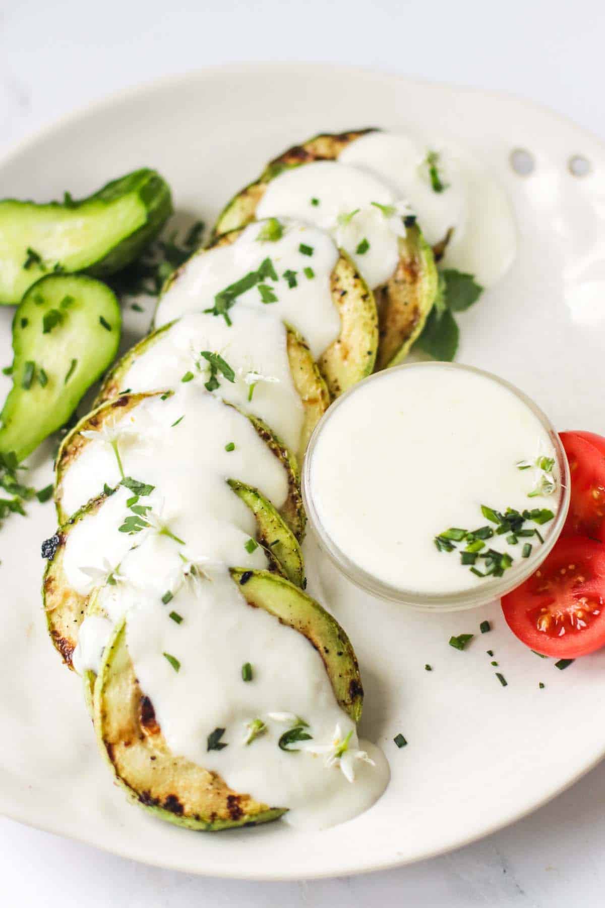 Cheese sauce in a bowl set on a white plate and drizzled over grilled zucchini.