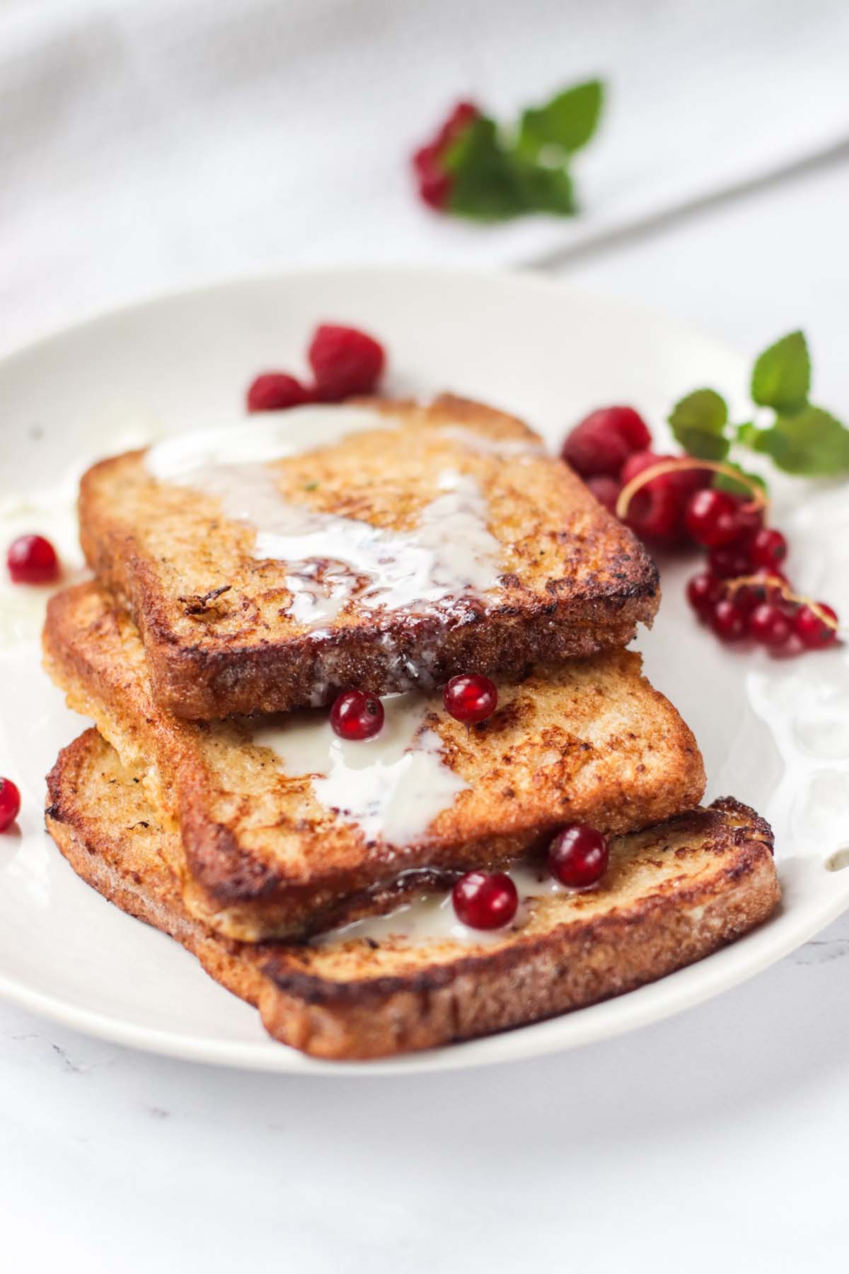 French toast on a plate with berries and drizzled with a white sauce.