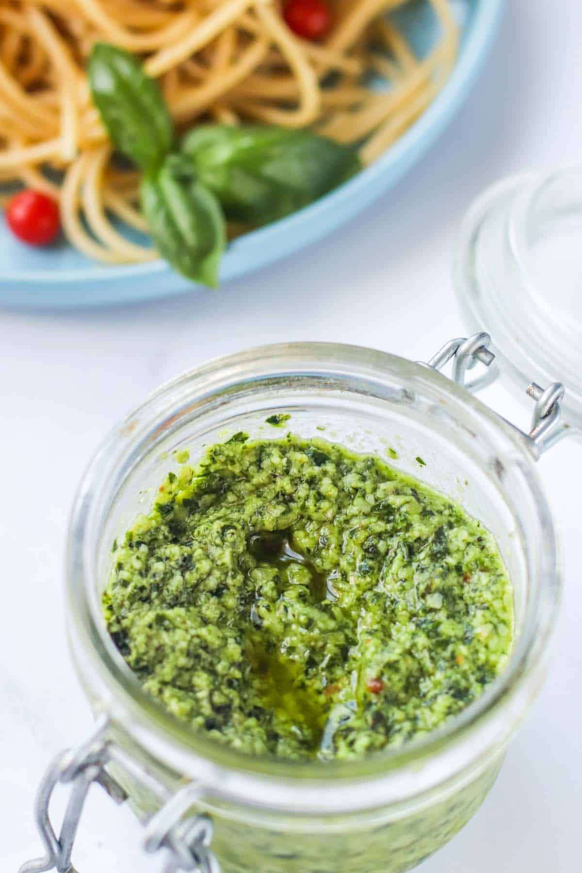 Pesto in a container in front of a plate of spaghetti.