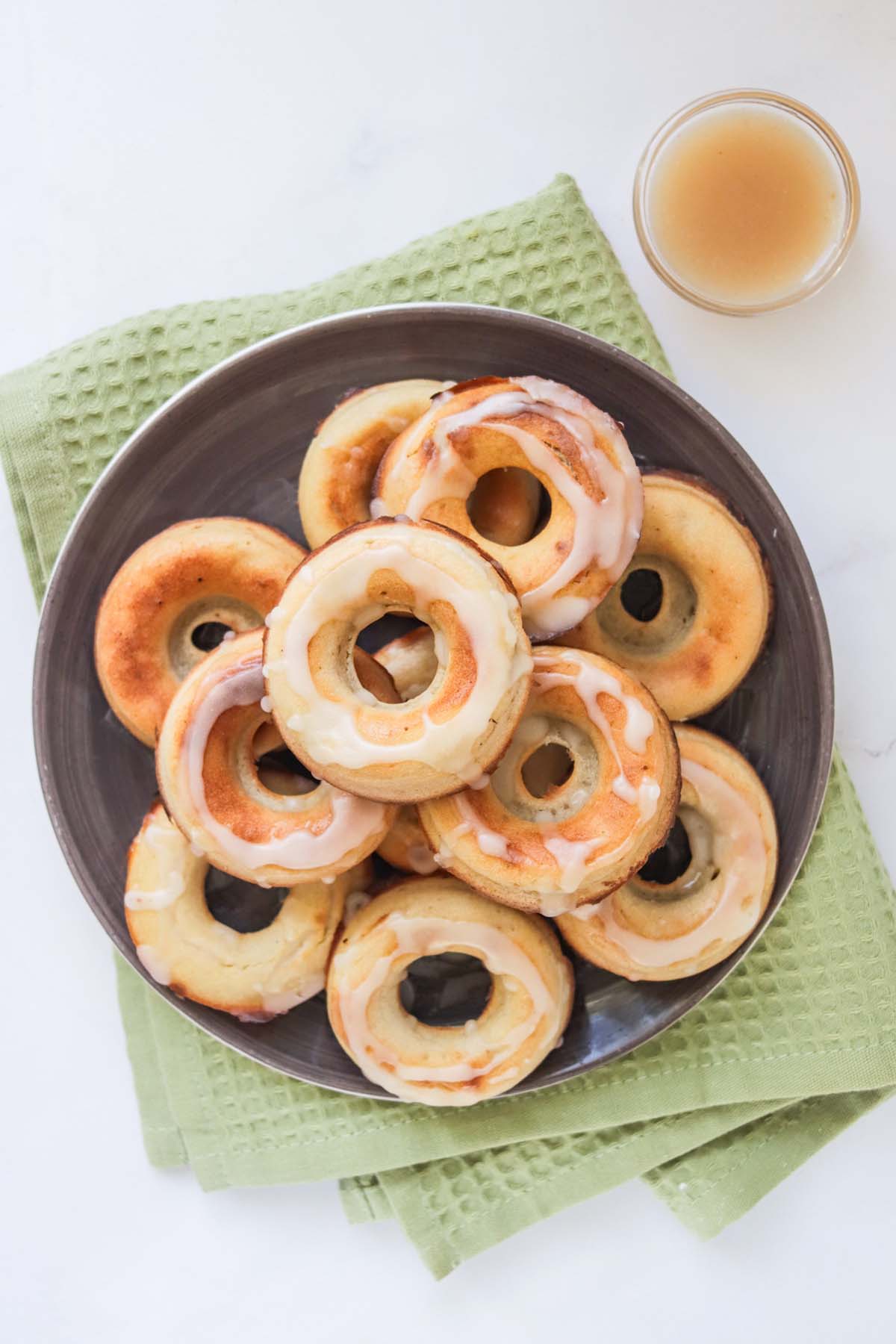 Donuts stacked on a black plate and set on a green kitchen towel.