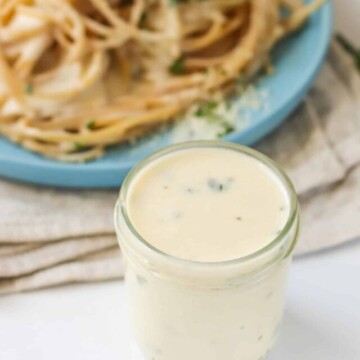 Sauce in a glass jar in from of a plate of pasta.