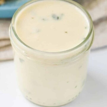 Sauce in a glass jar in from of a plate of pasta.