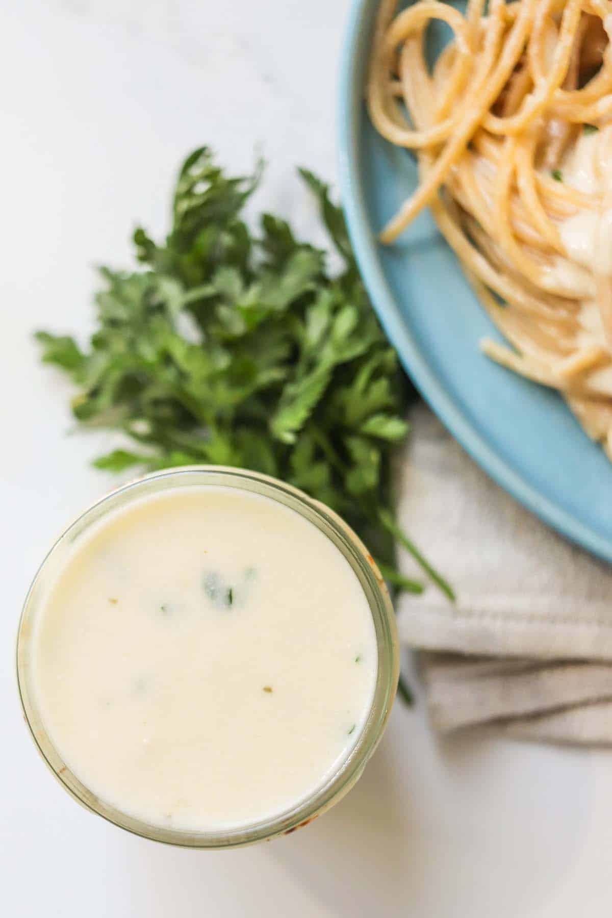 Alfredo sauce in a jar next to fresh parsley.