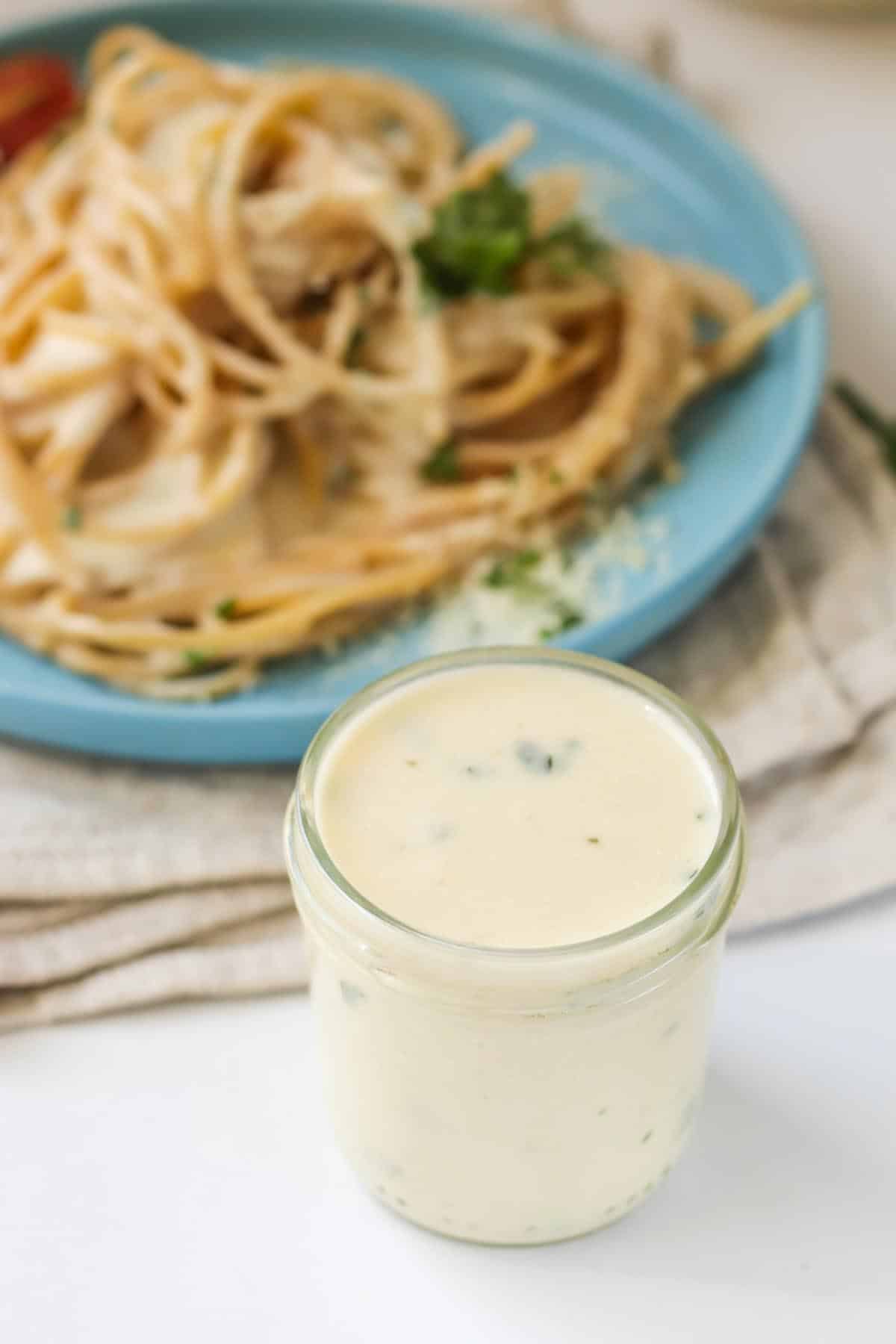 Sauce in a glass jar in from of a plate of pasta.