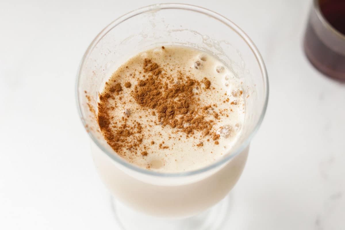 A latte in a glass with cinnamon powder on top.
