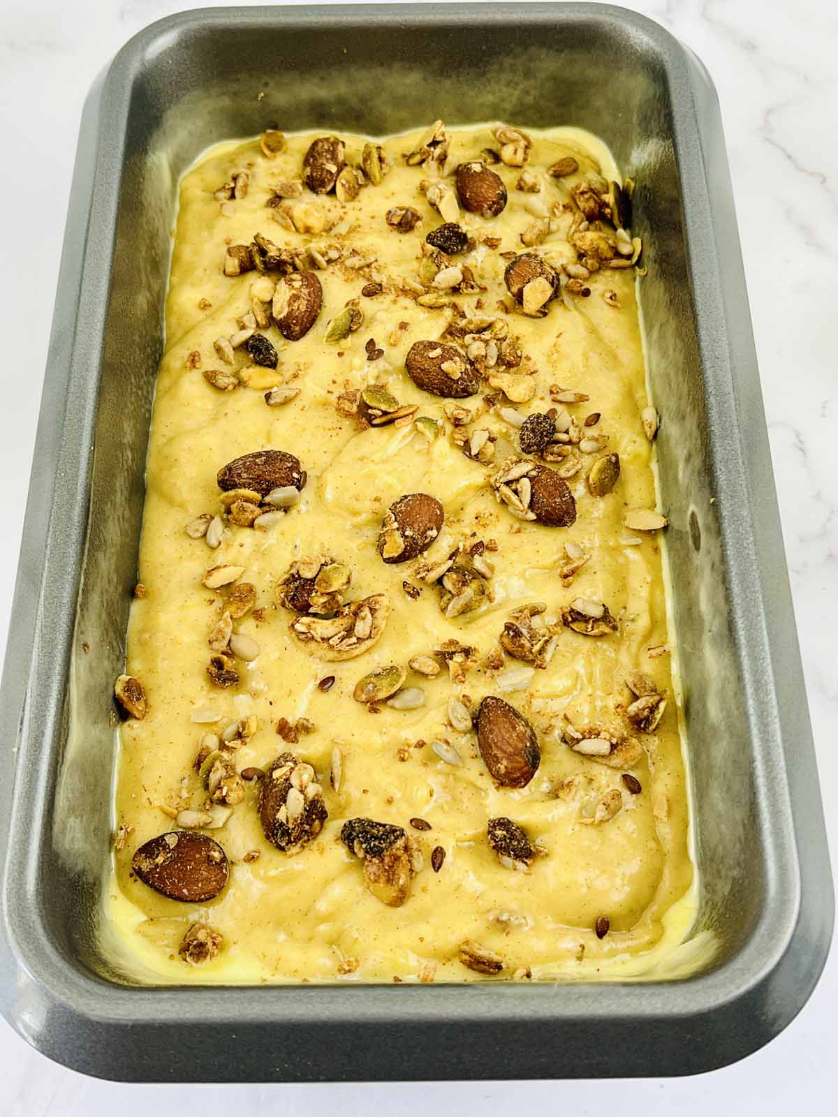 Bread batter in a loaf pan topped with chopped nuts.