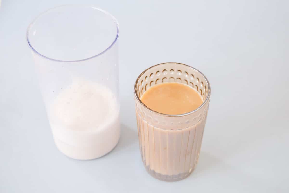 Milk in a glass next to coffee in a glass.