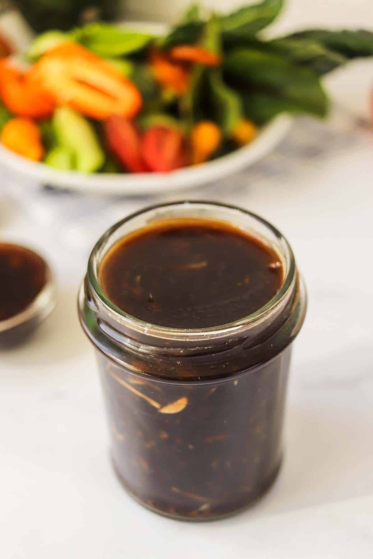 Sauce in a jar in front of a plate of vegetables.