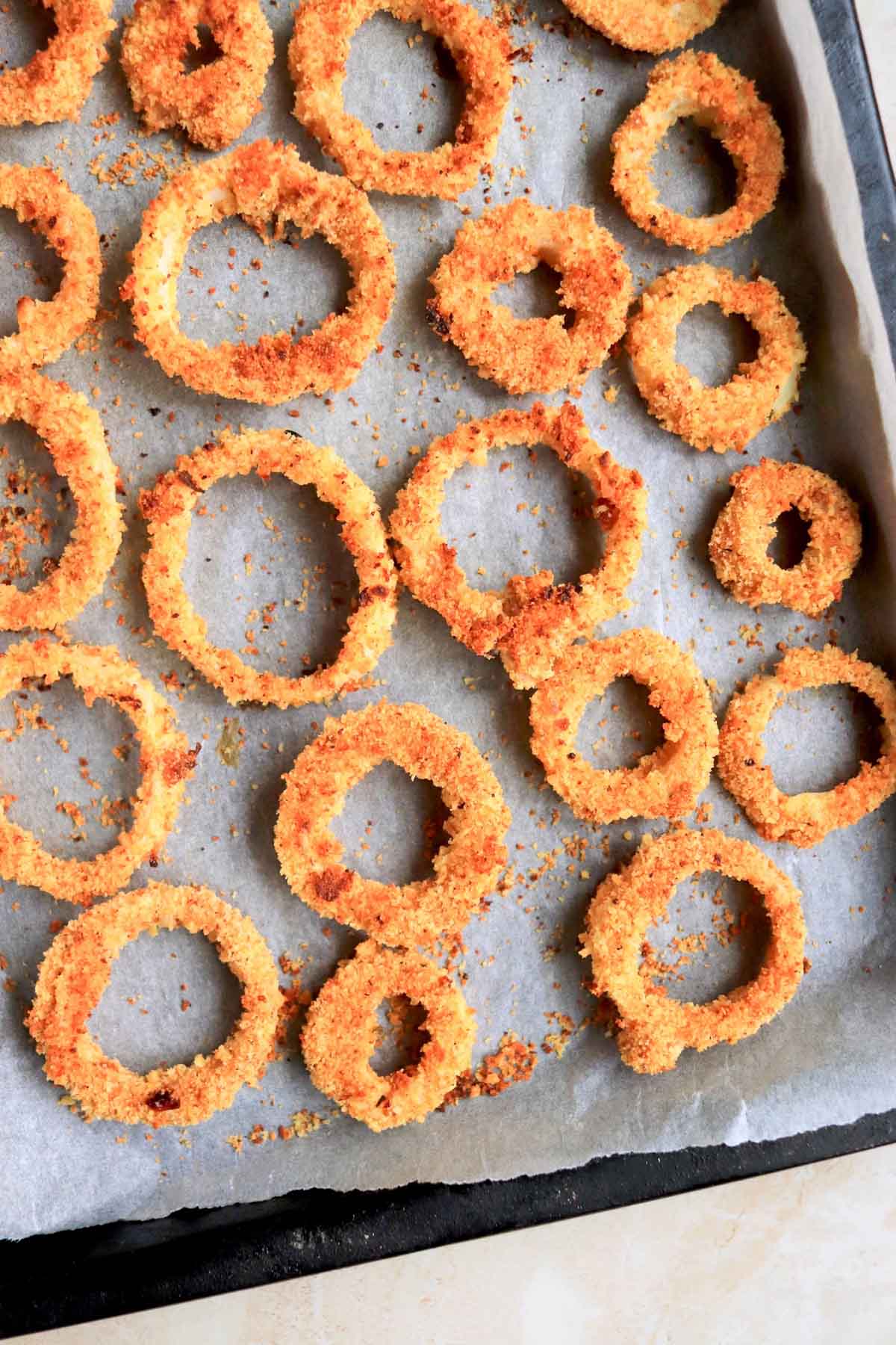 Baked onion rings on a parchment lined baking sheet.