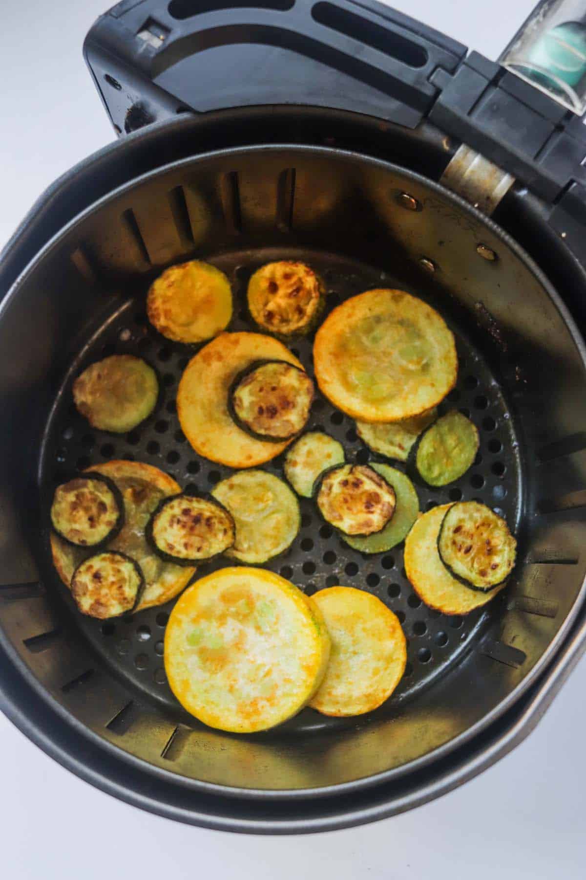 Cooked slices of squash in the air fryer basket.