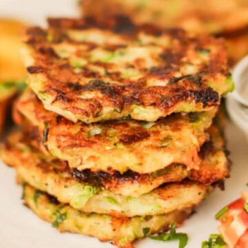 Zucchini fritters stacked on a plate next to a dipping sauce.