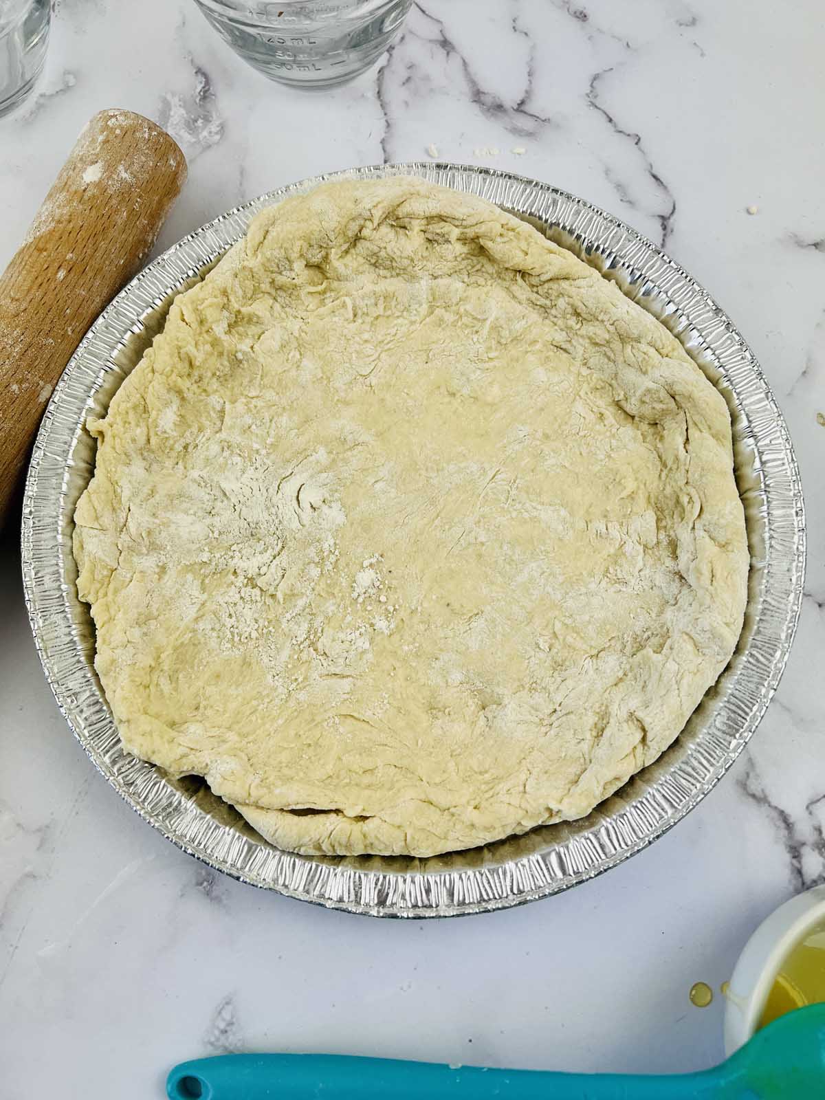 The pie dough spread out into a pie tin.