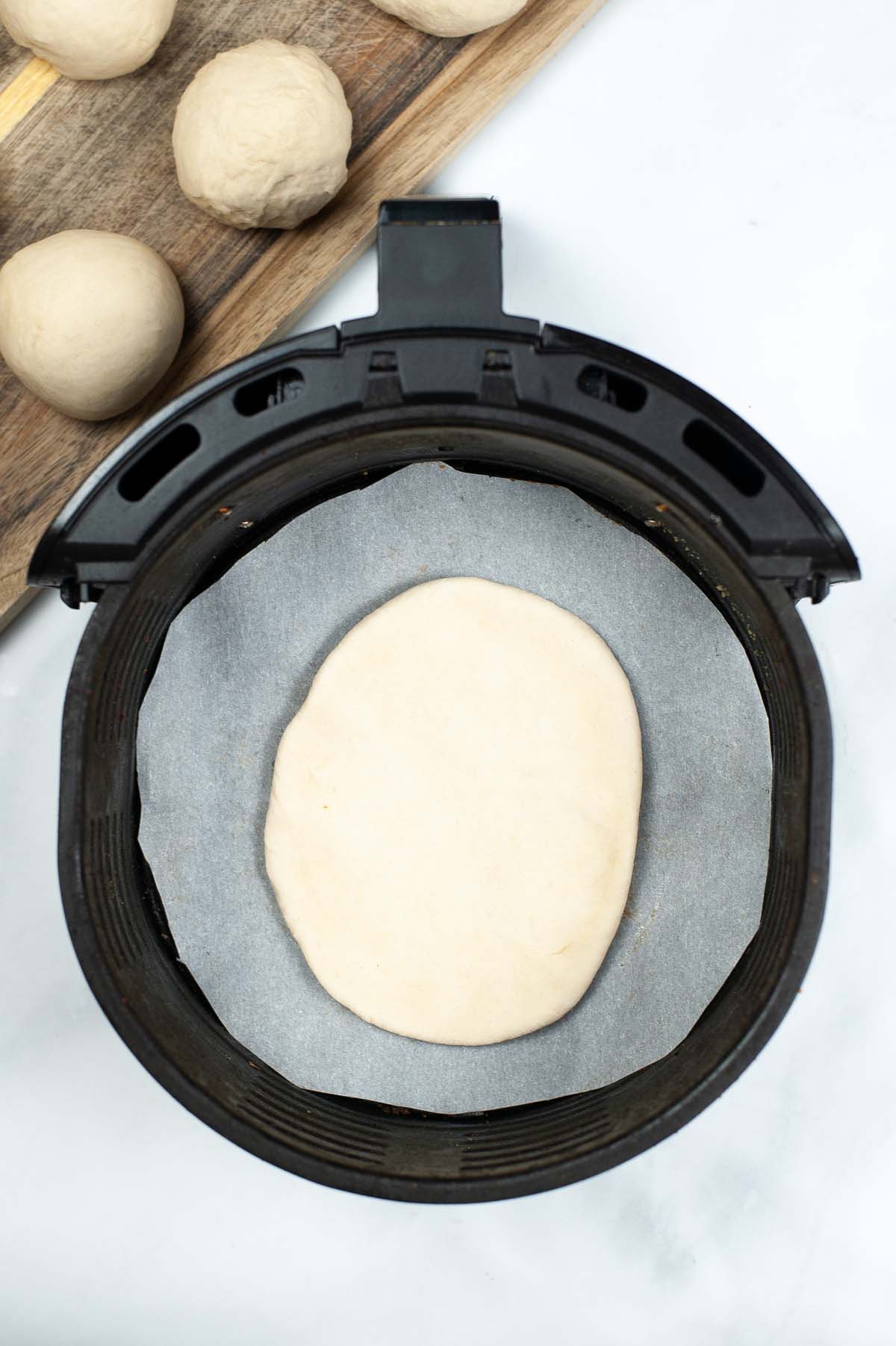 A flat disc of dough in the air fryer basket lined with parchment paper.