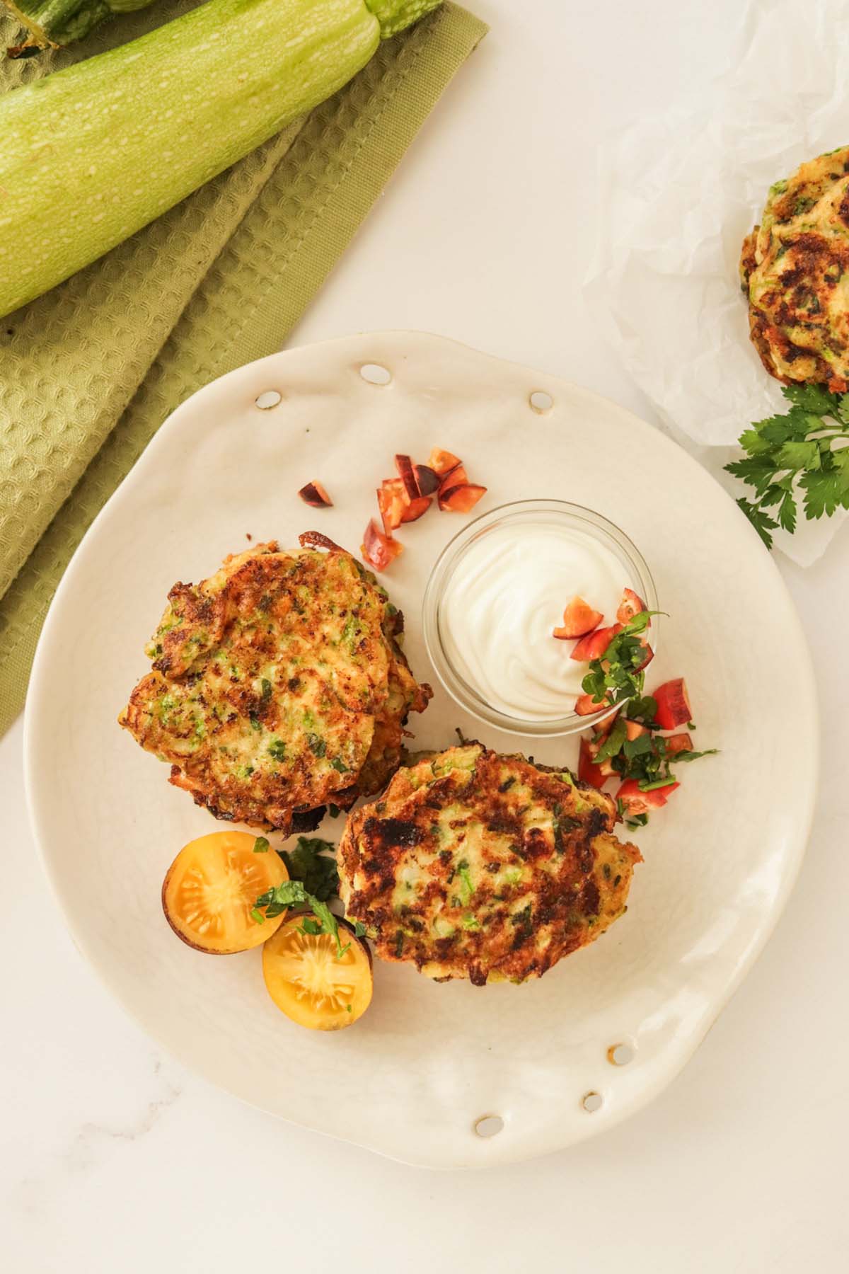 Fritters on a plate with dipping sauce and tomatoes.