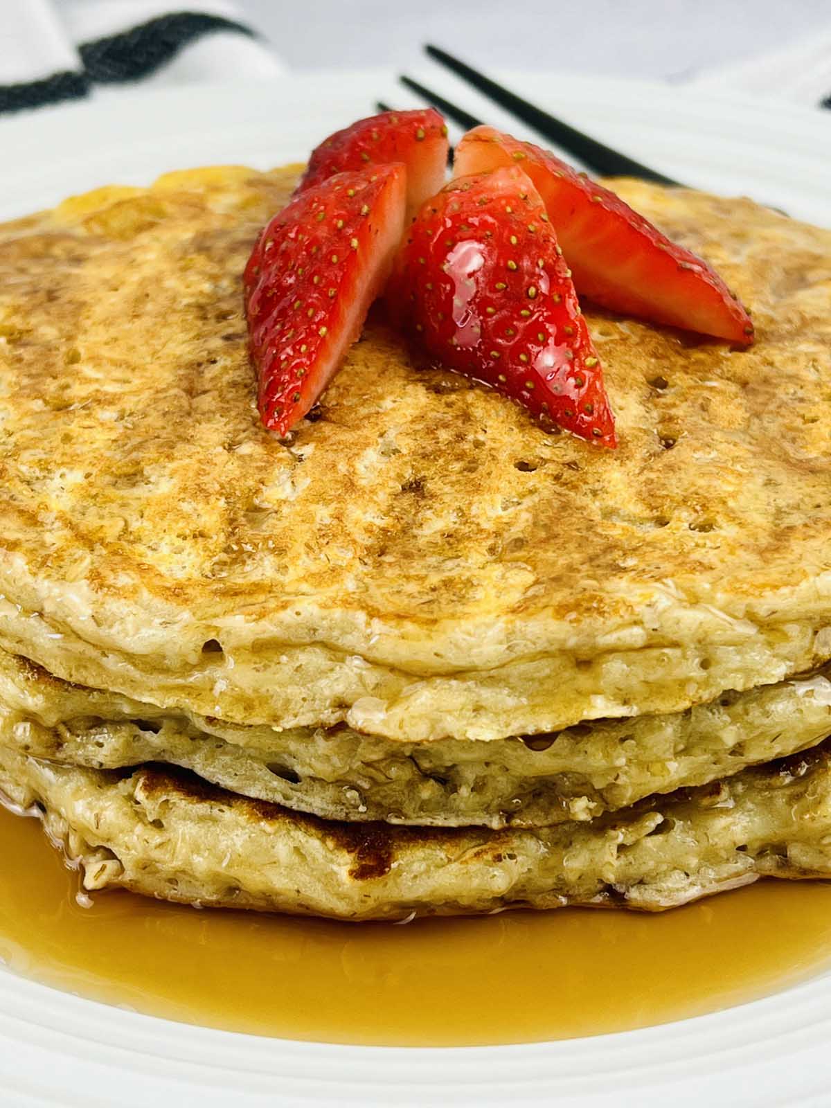Pancakes on a plate topping with slices of strawberries.
