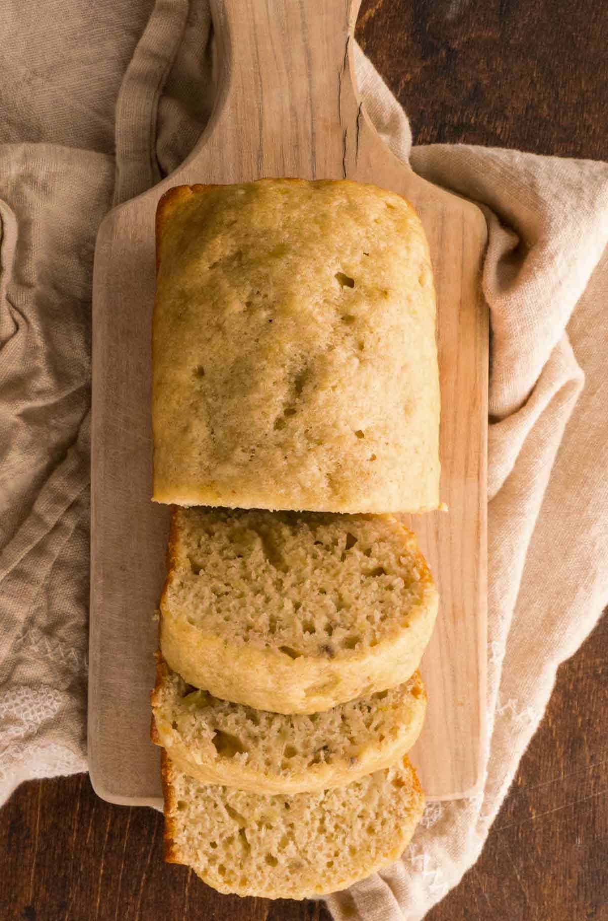 Sliced banana bread on a cutting board that is sitting on a kitchen towel.