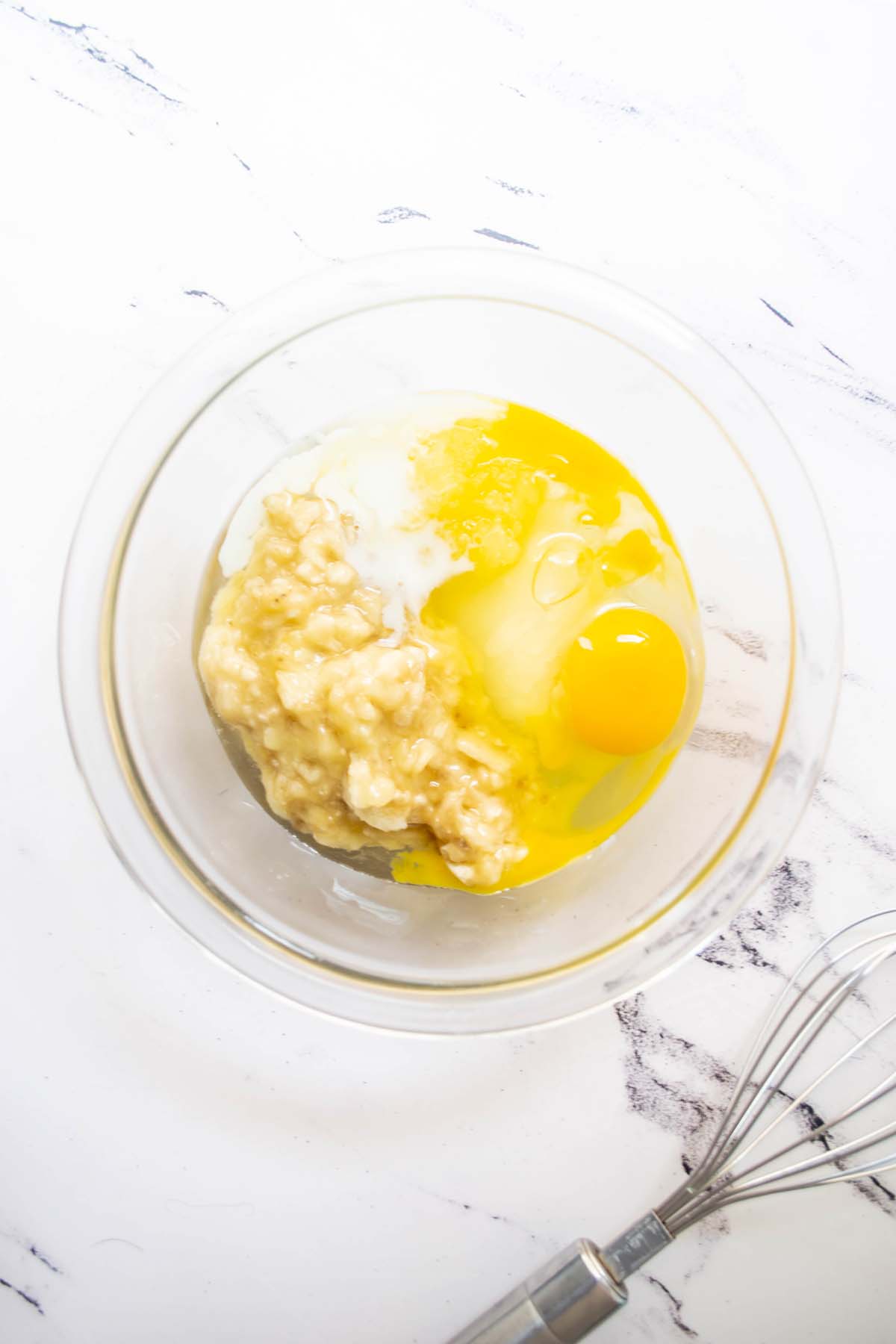 Mashed bananas, milk and eggs in a bowl.